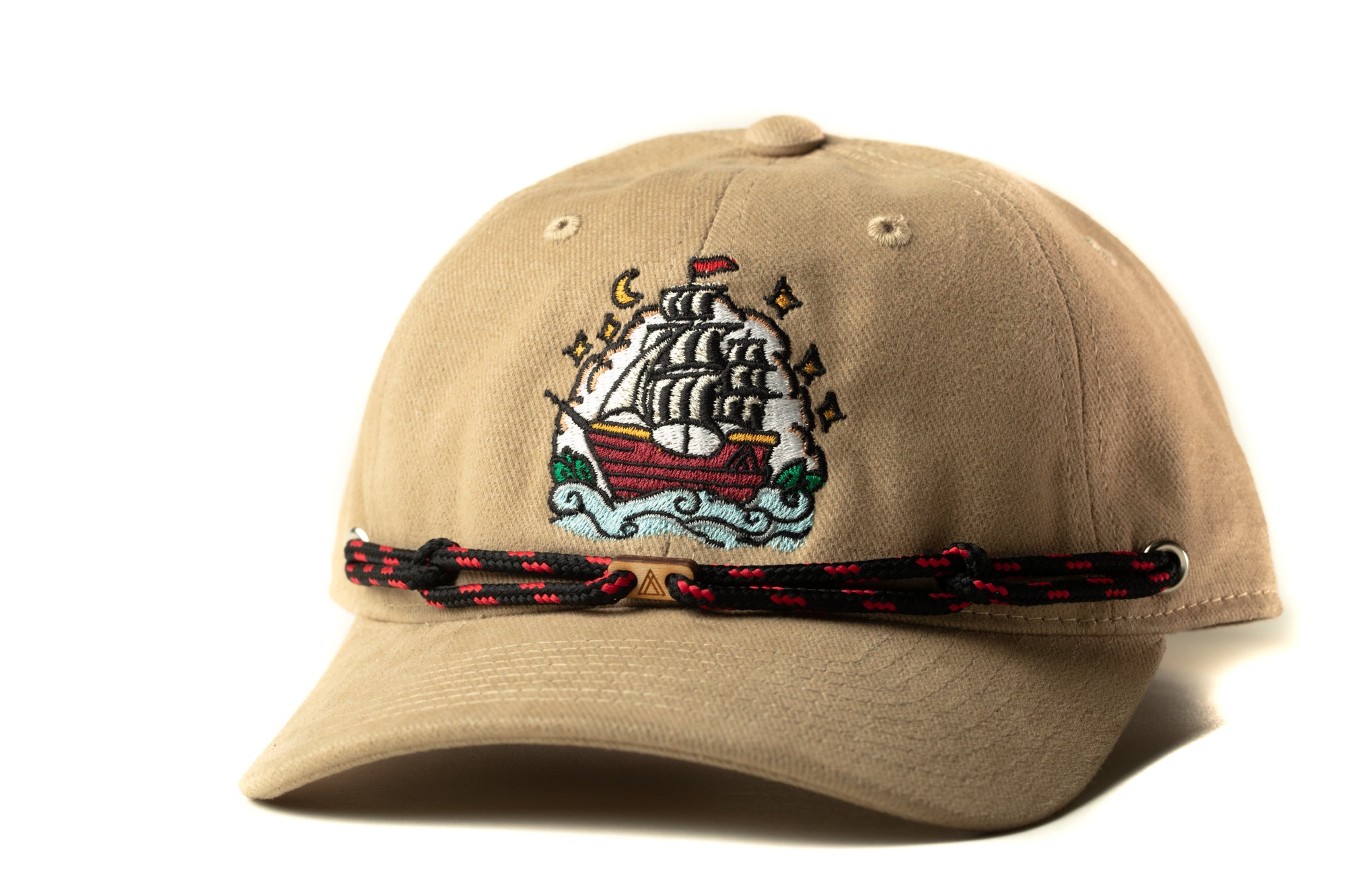 A beige baseball cap with a colorful embroidered design depicting a ship on the front.