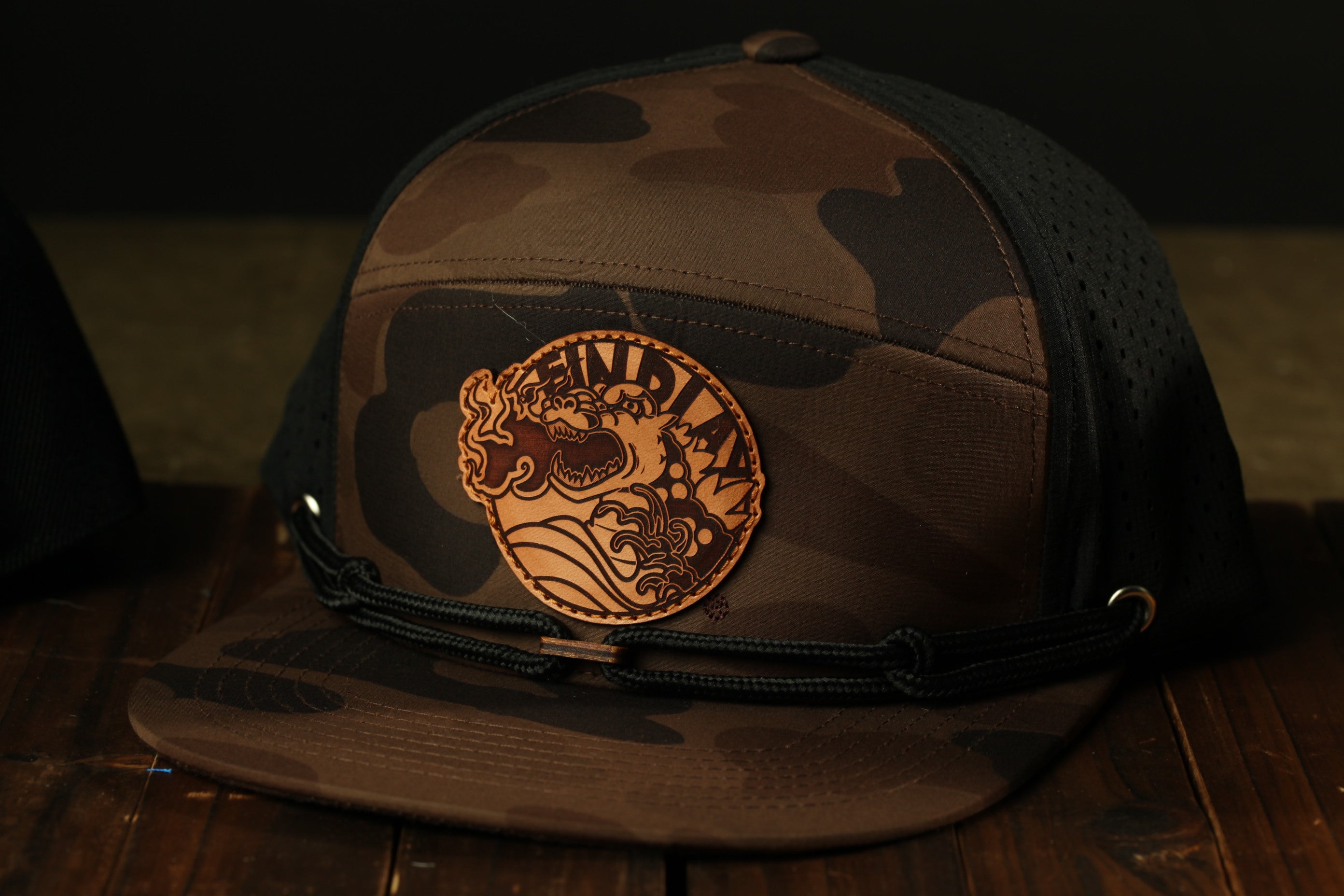 A camouflage baseball cap with a circular patch on the front displaying a graphic design.