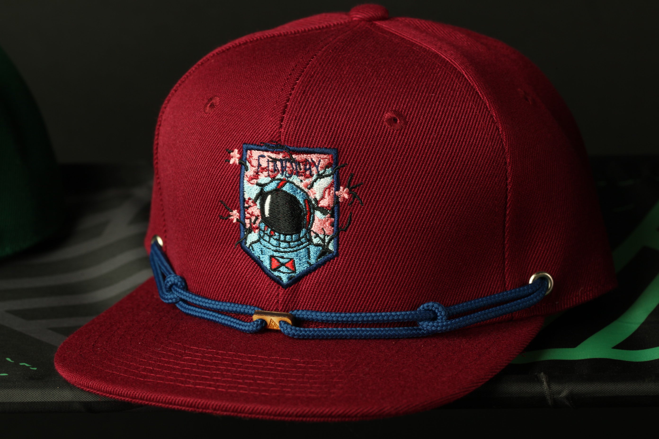 A red baseball cap with a blue adjustable strap and a patch featuring a space helmet design.