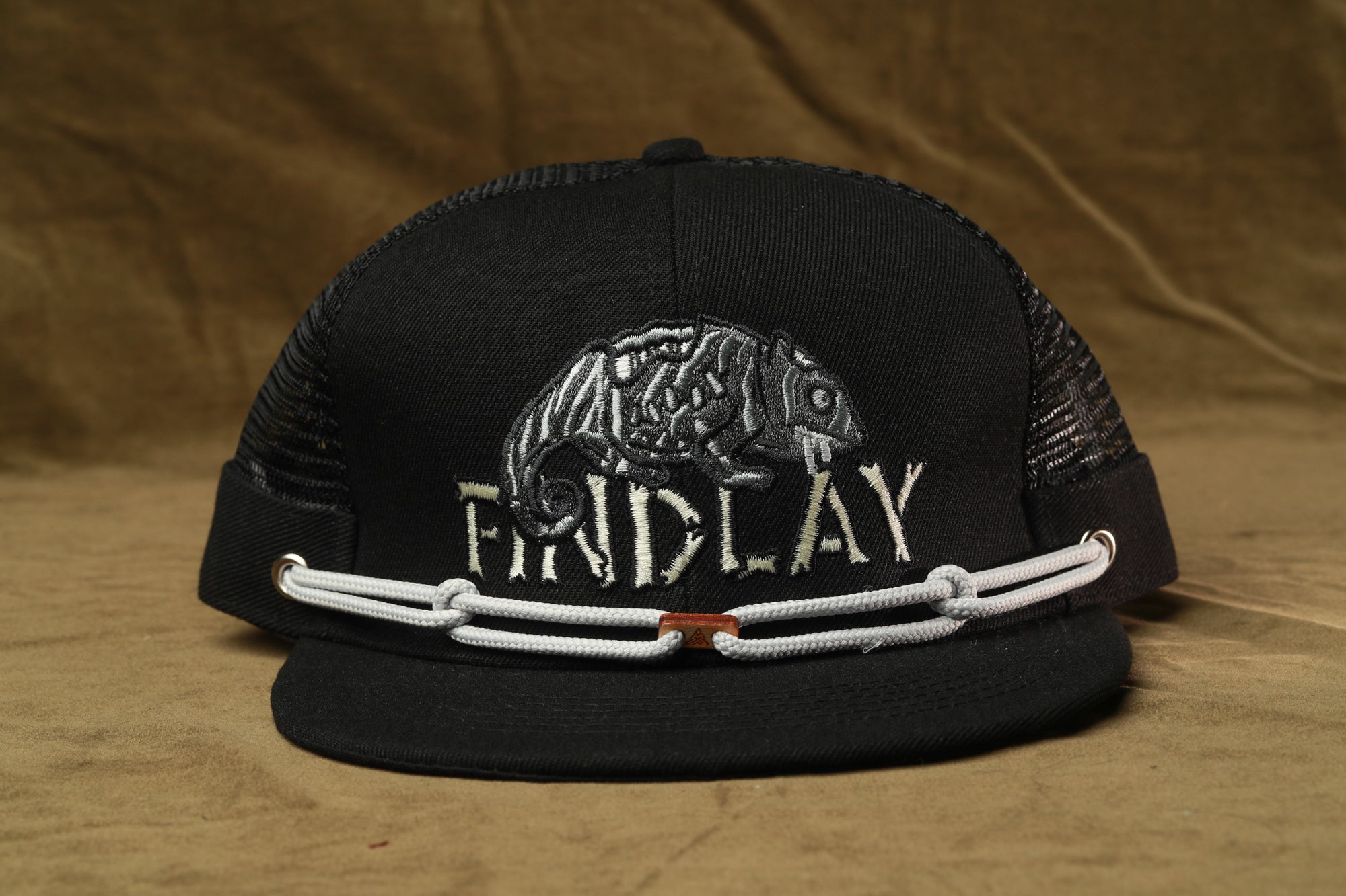 A black baseball cap with a mesh panel and a white chain strap.