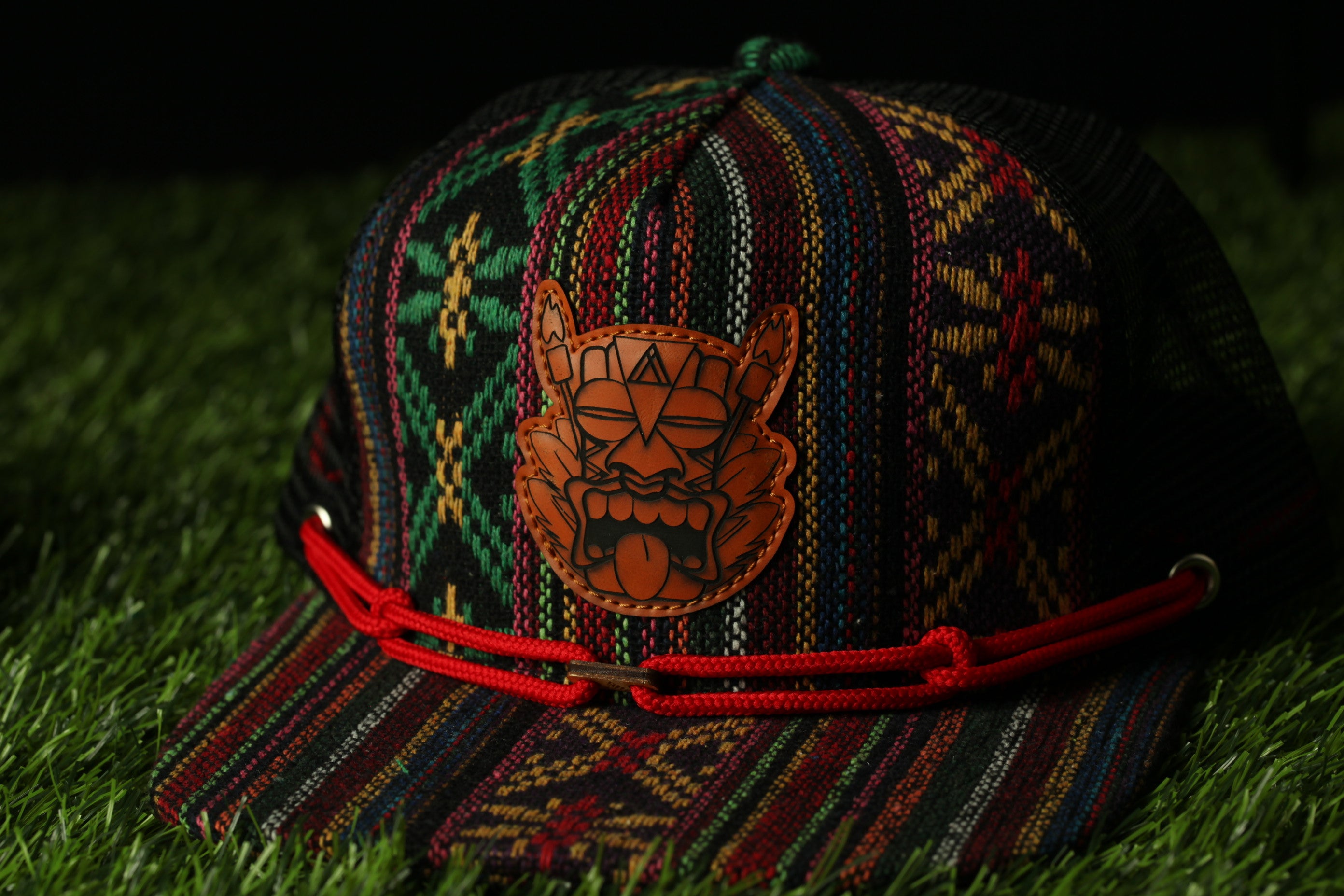 A colorful, patterned baseball cap with a distinctive orange and black design on the front, resting on a grassy surface.