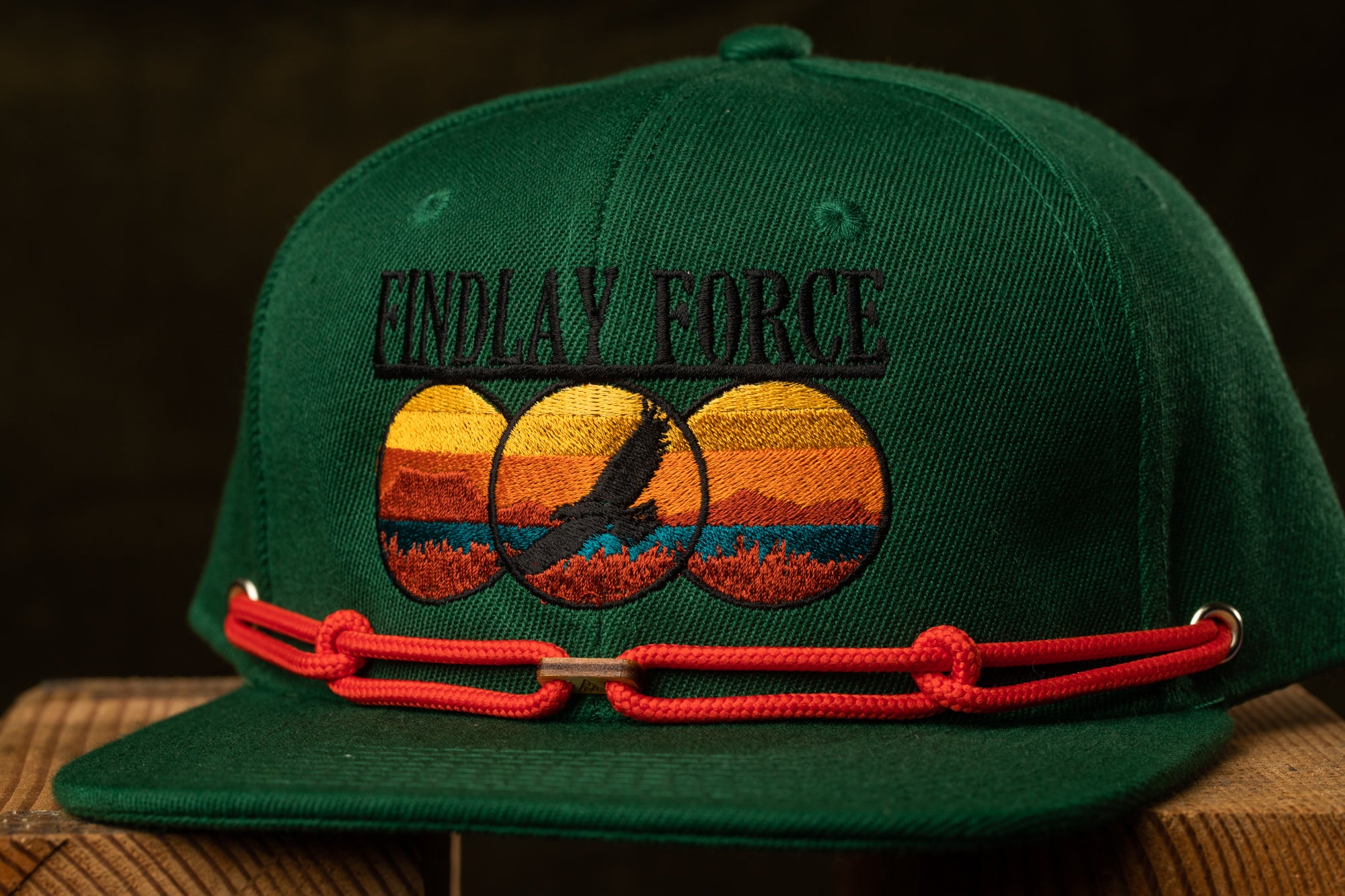 A green baseball cap with a red chain strap and a graphic design on the front.