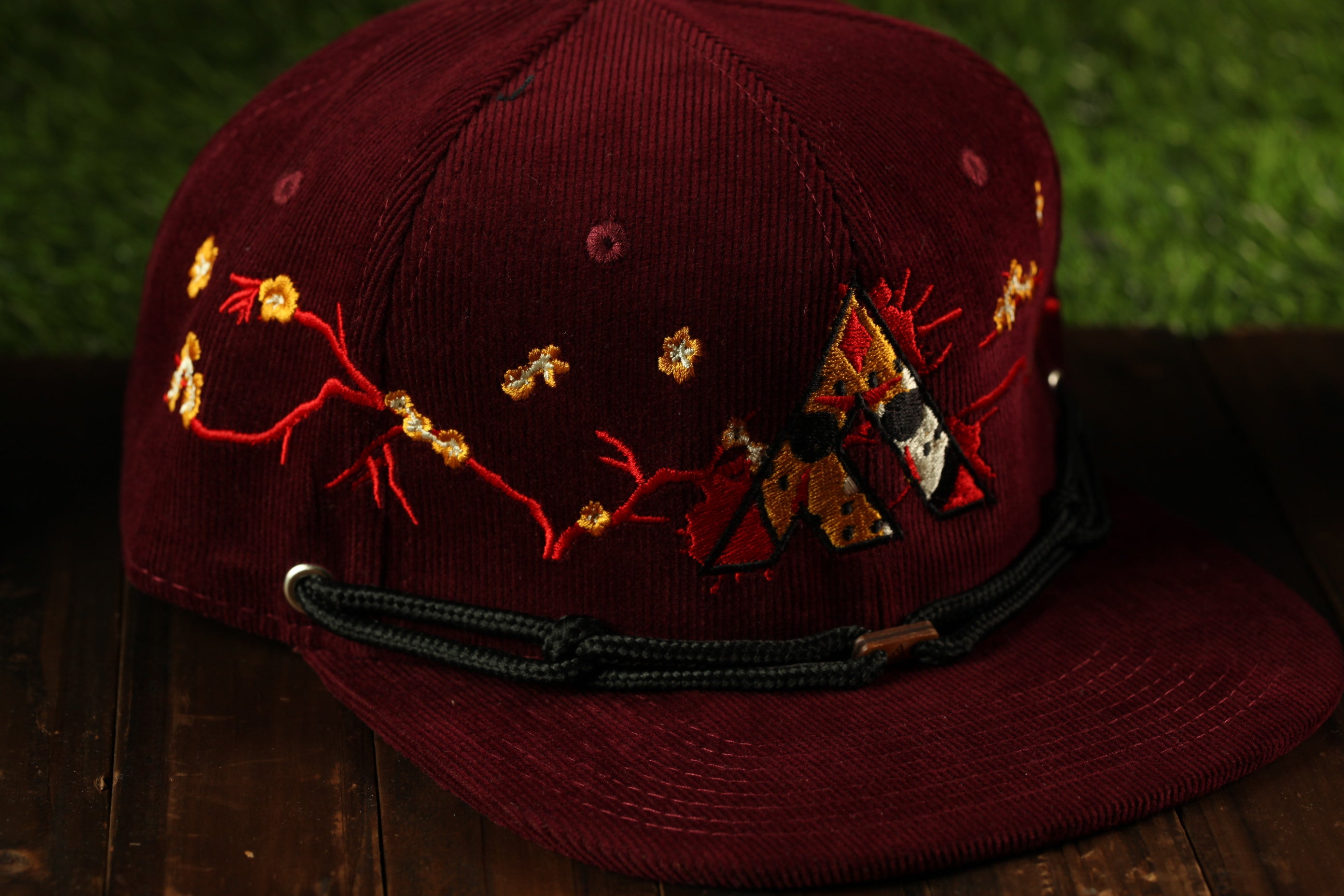 A burgundy baseball cap with a black band and embroidered designs on the front.
