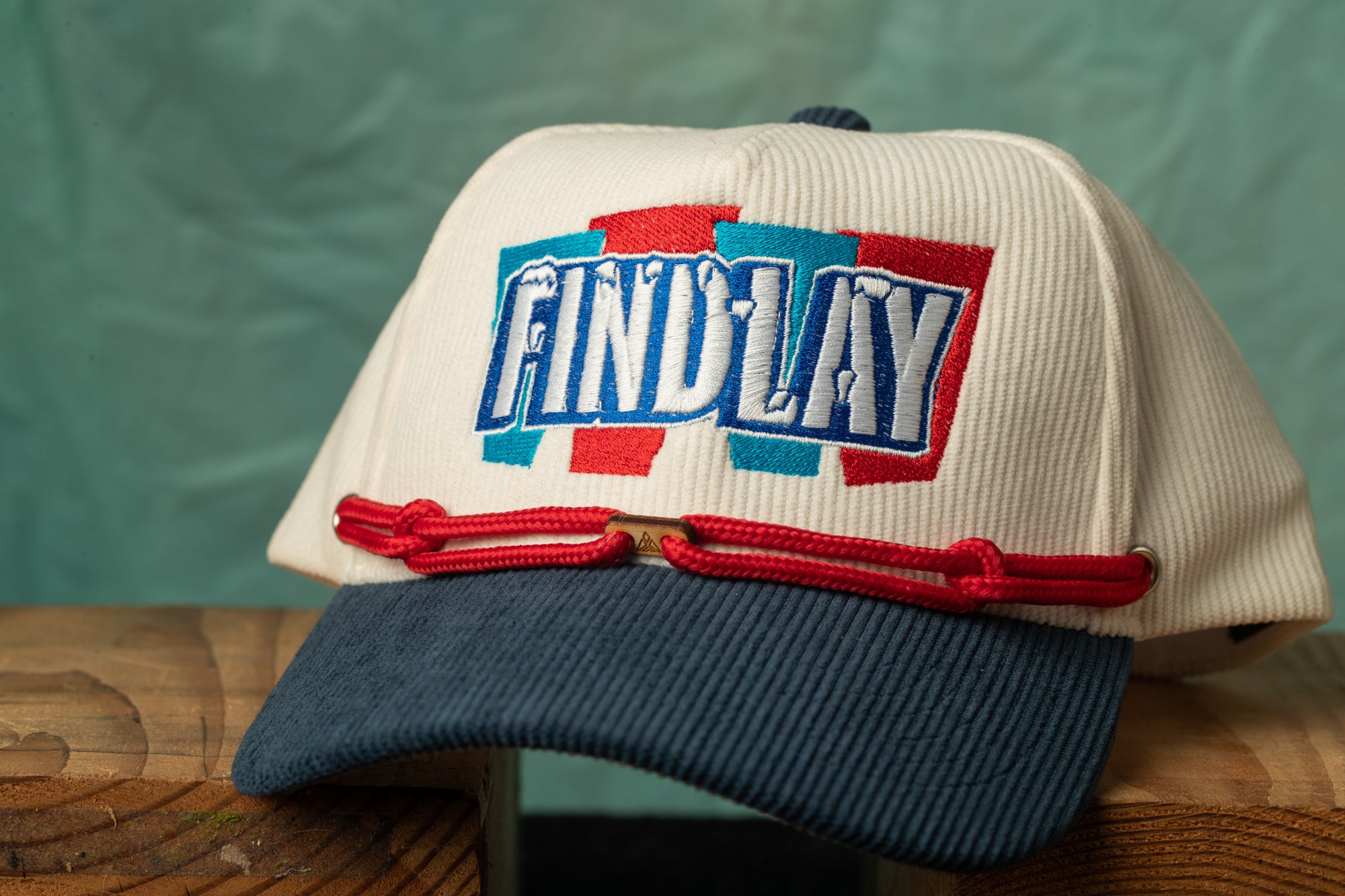 A white baseball cap with the word "FINDA" embroidered on it, sitting on a wooden surface.