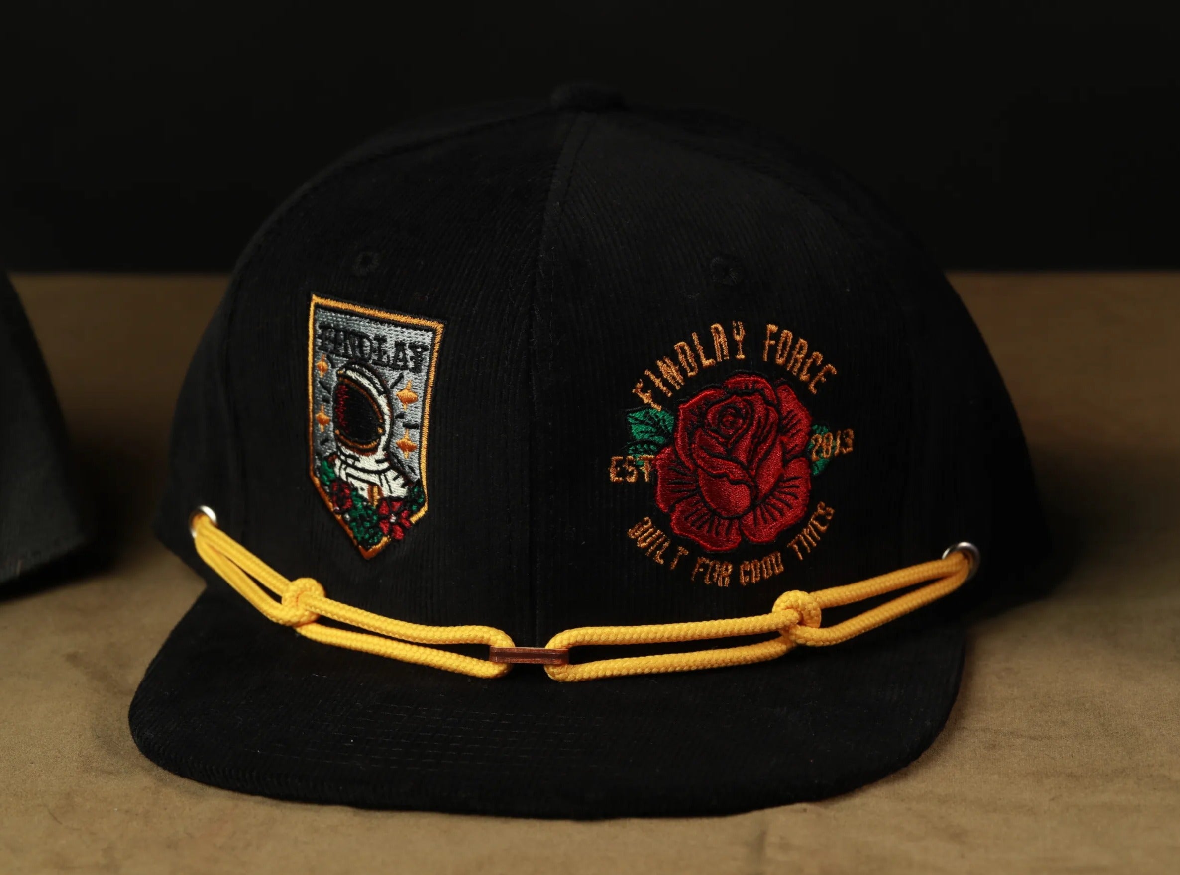 A black baseball cap with yellow strings and two embroidered patches on the front.