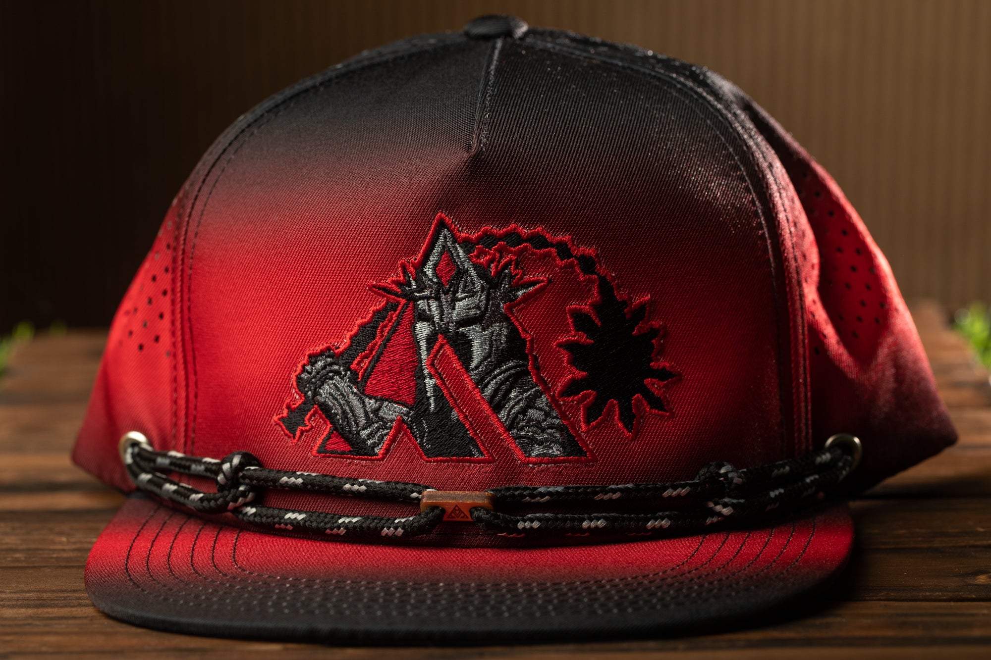 A red baseball cap with a black and red logo on the front, sitting on a wooden surface.