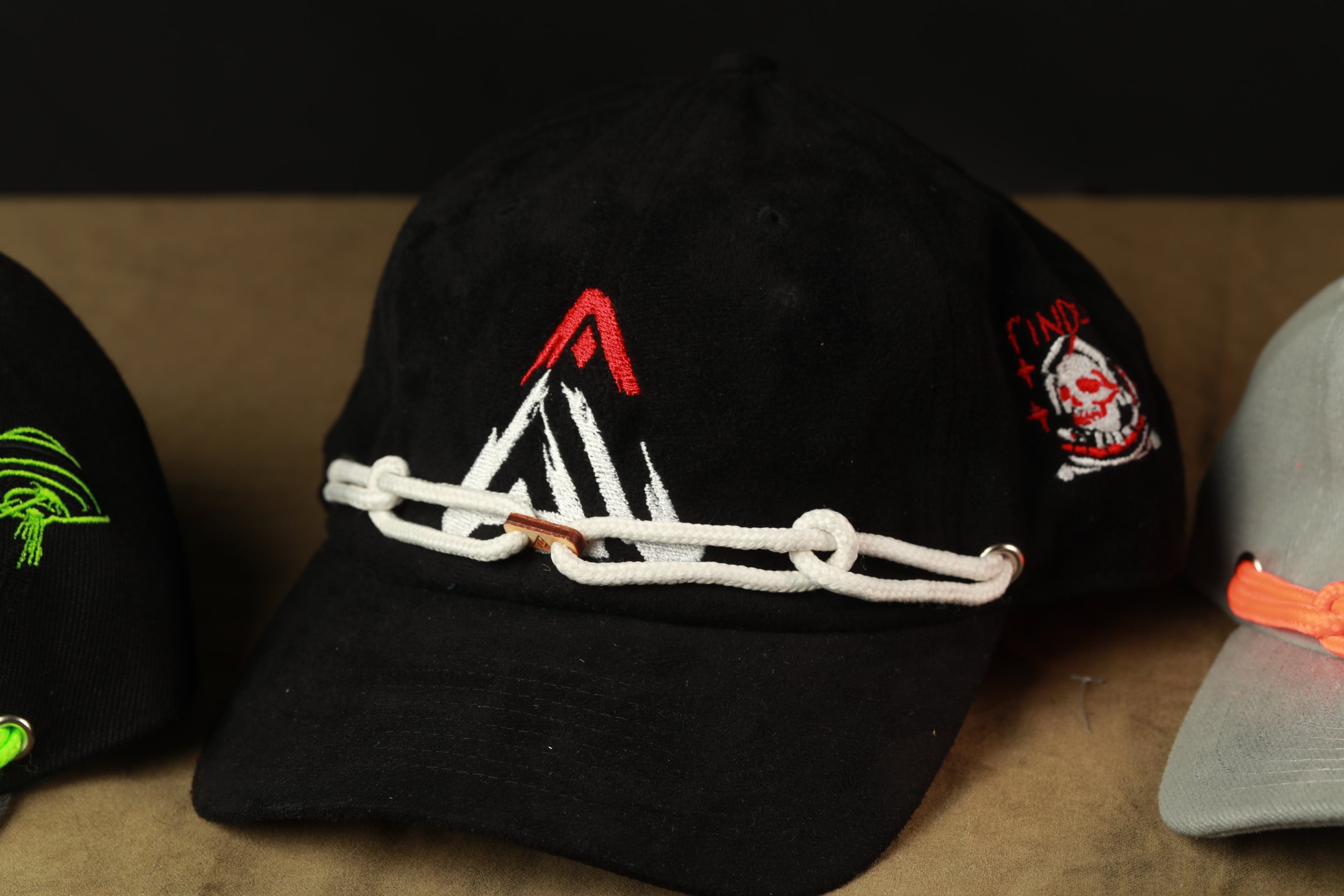 A close-up view of a black baseball cap with a red and white logo, placed on a surface next to other hats.