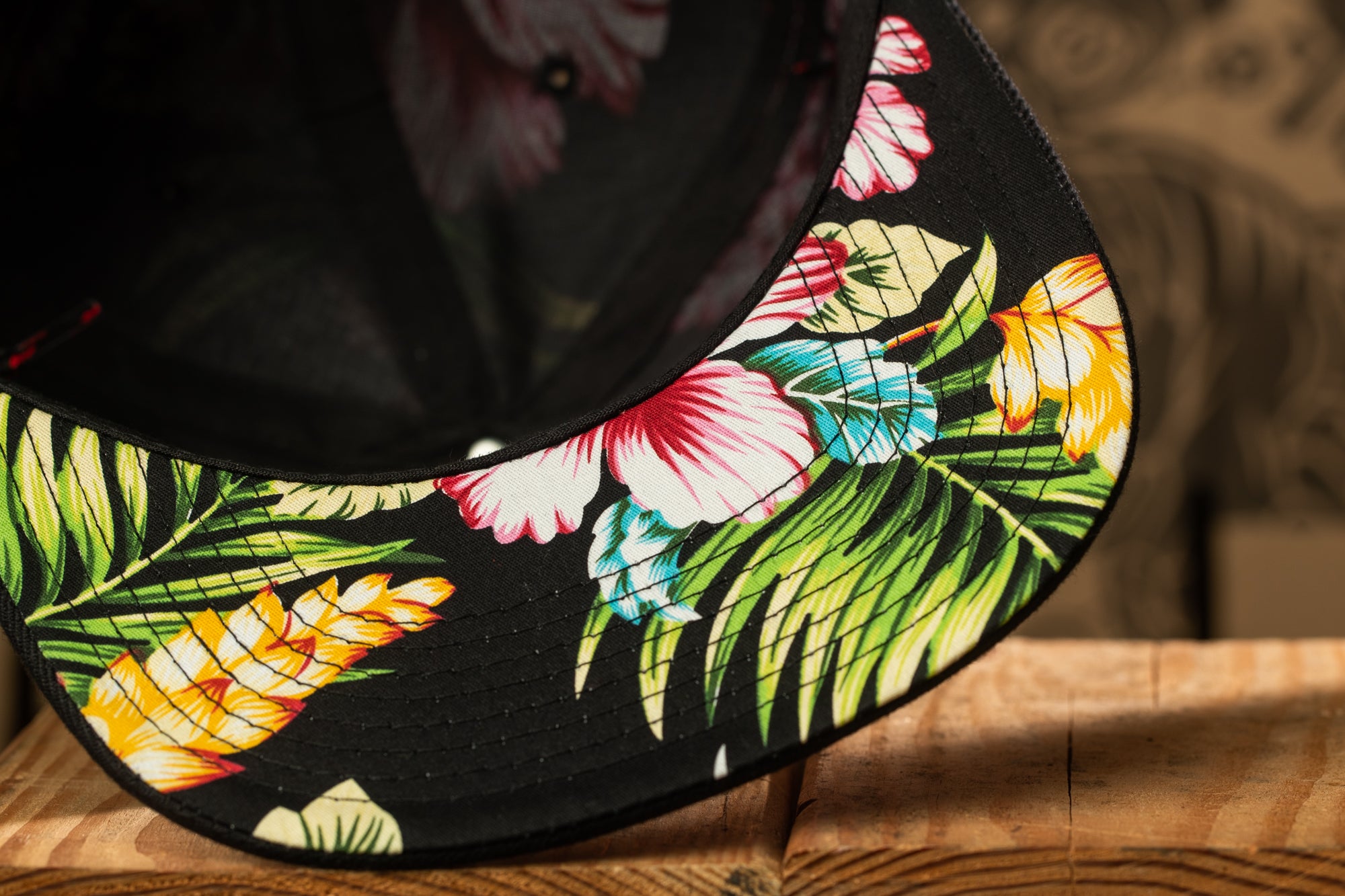 a close-up view of a black baseball cap with a colorful floral pattern on the brim.