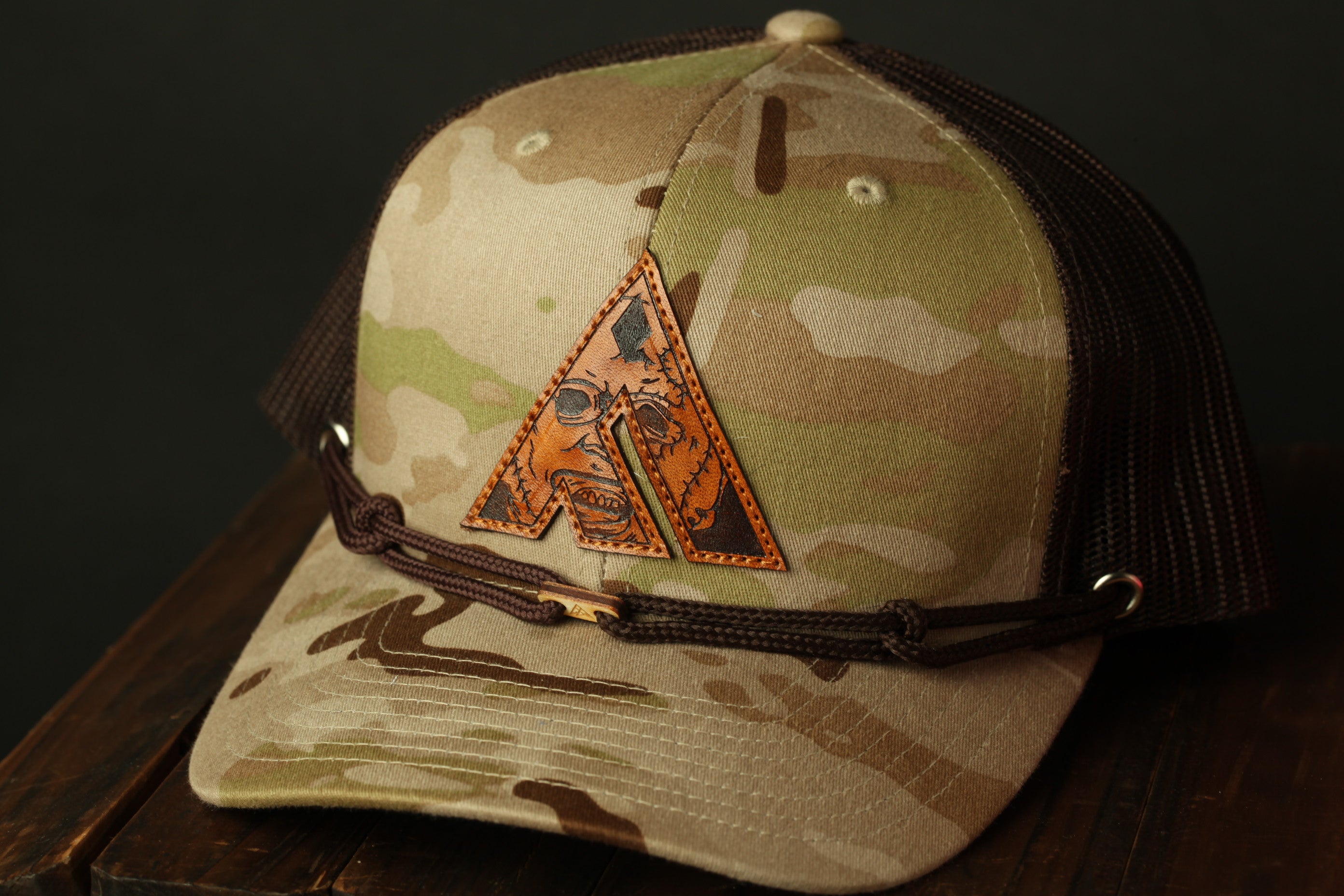 A camouflage baseball cap with a leather patch featuring an orange triangle design.