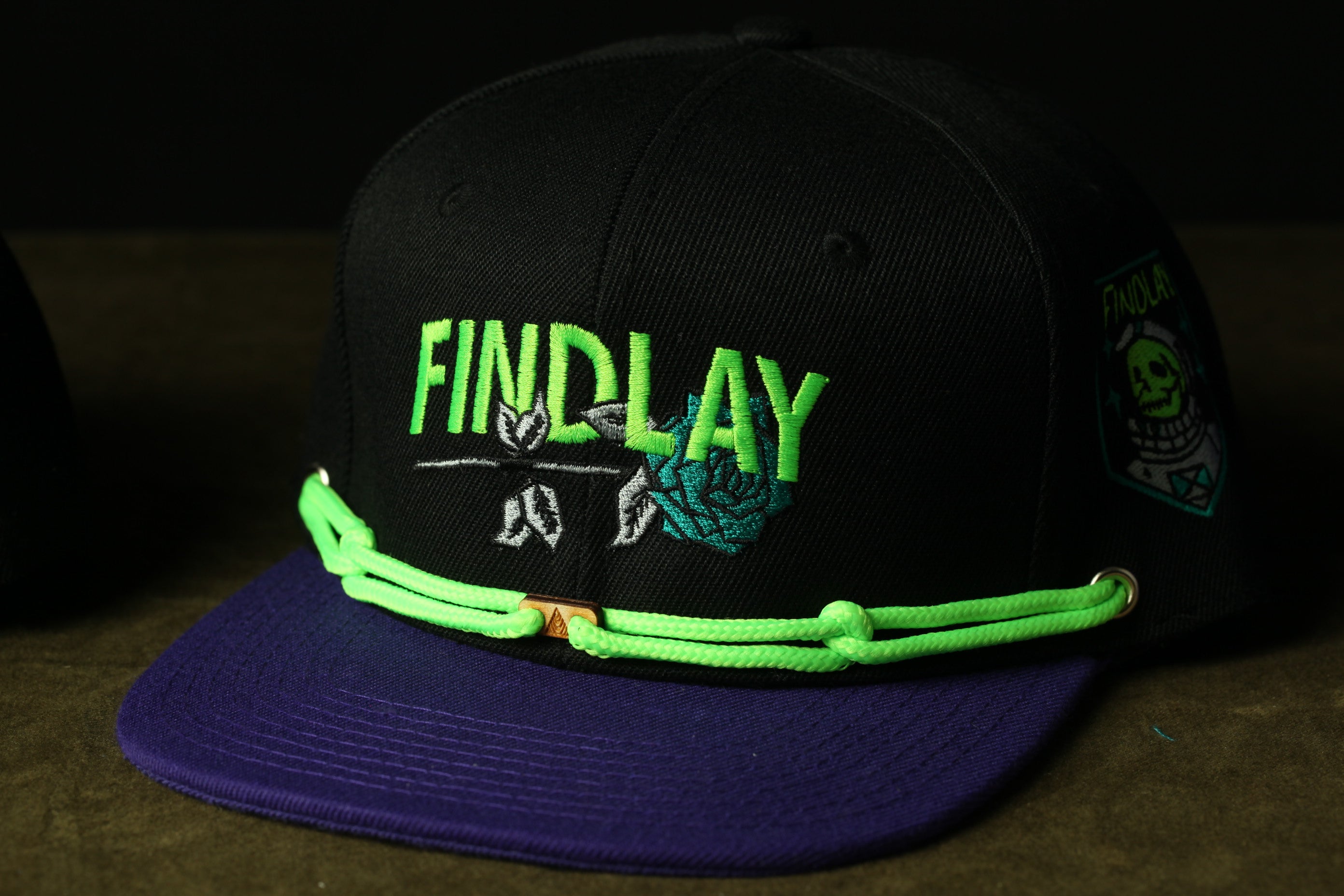 A black baseball cap with the word "FINDlay" printed on it in green and purple colors, along with a skull and crossbones design.
