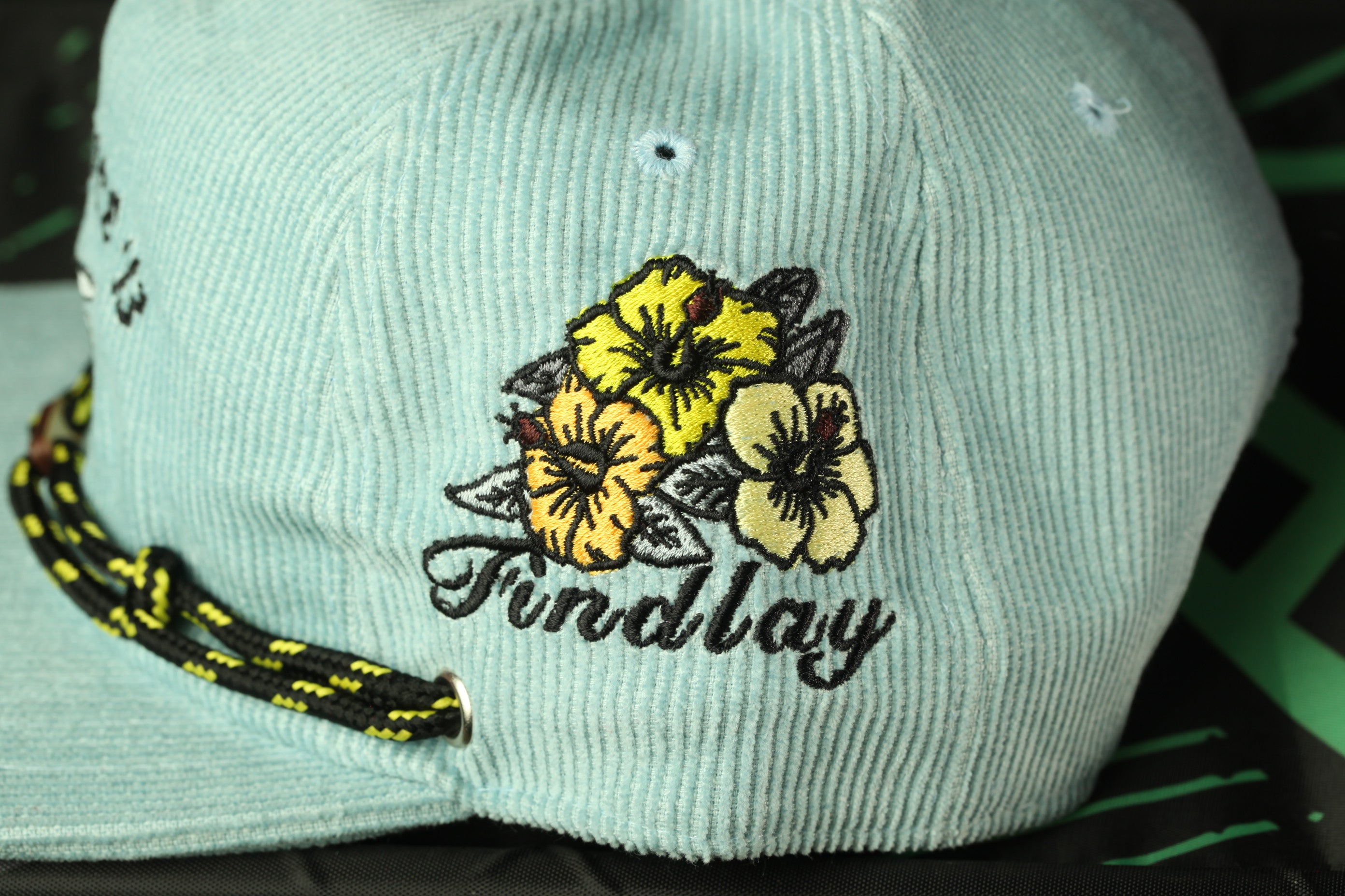 A close-up of a light blue baseball cap with a floral embroidered design and the word "Finlay" printed on it.