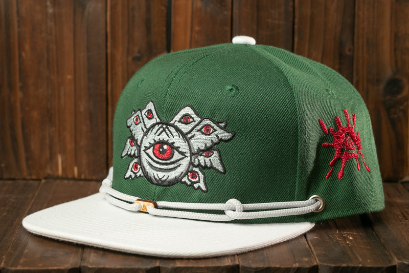 A green baseball cap with a white brim and a white band, featuring a unique design with a central eye surrounded by multiple smaller eyes.