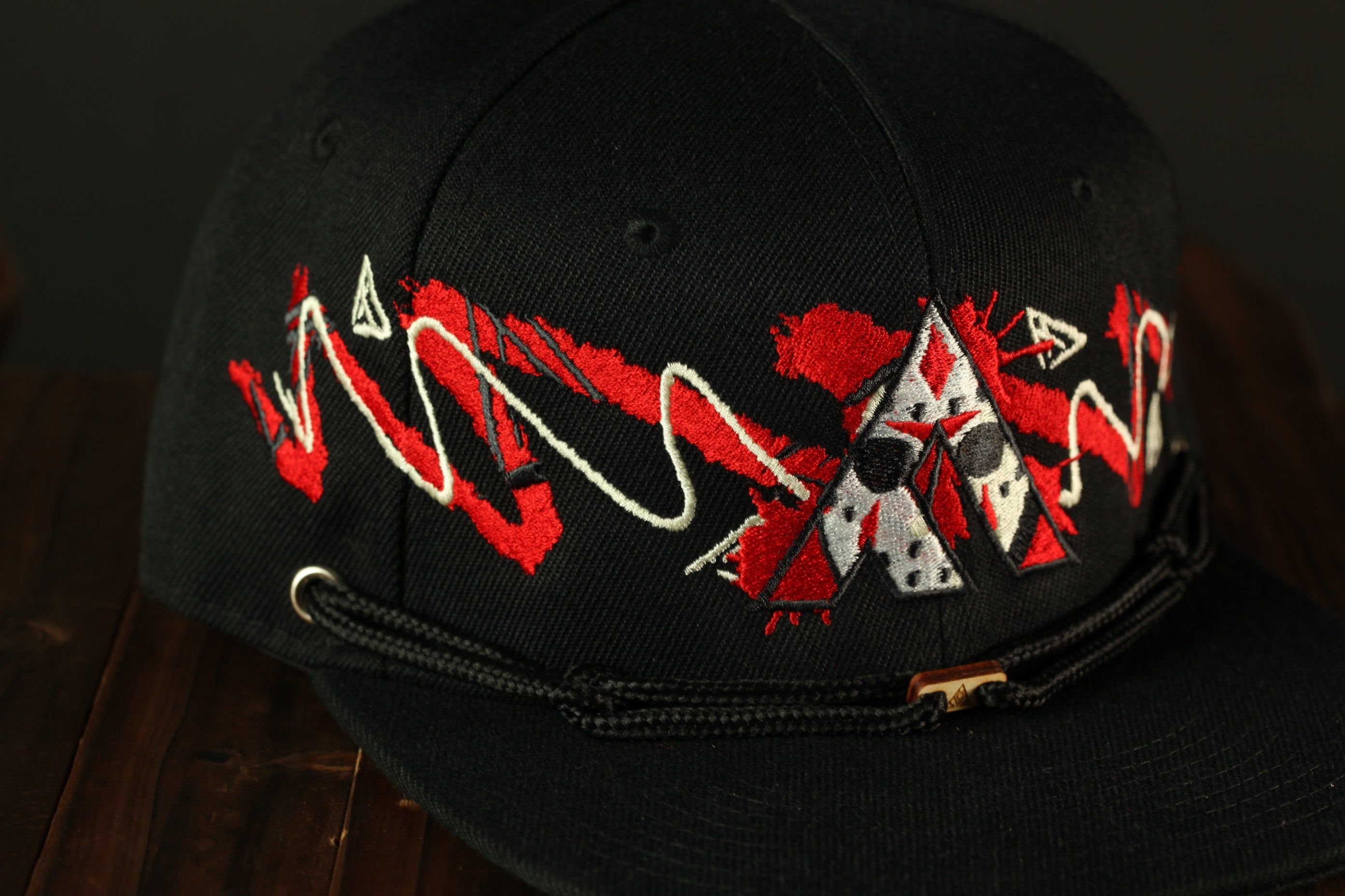 A close-up view of a black baseball cap with a red and white design featuring a stylized face and geometric shapes.