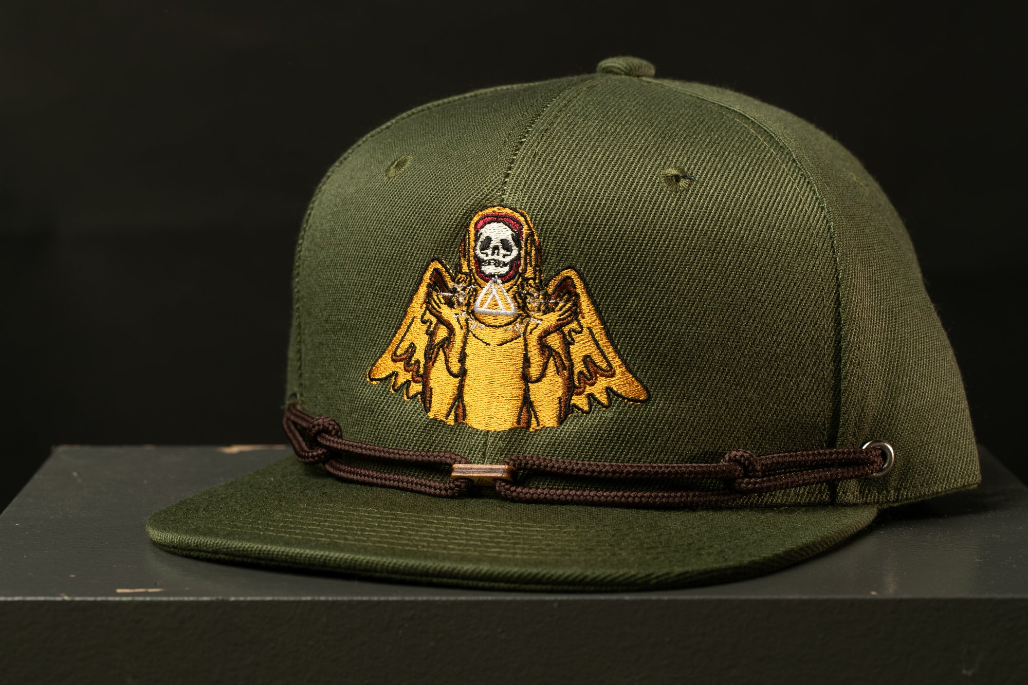 A green baseball cap with a graphic of a skull and wings on the front.