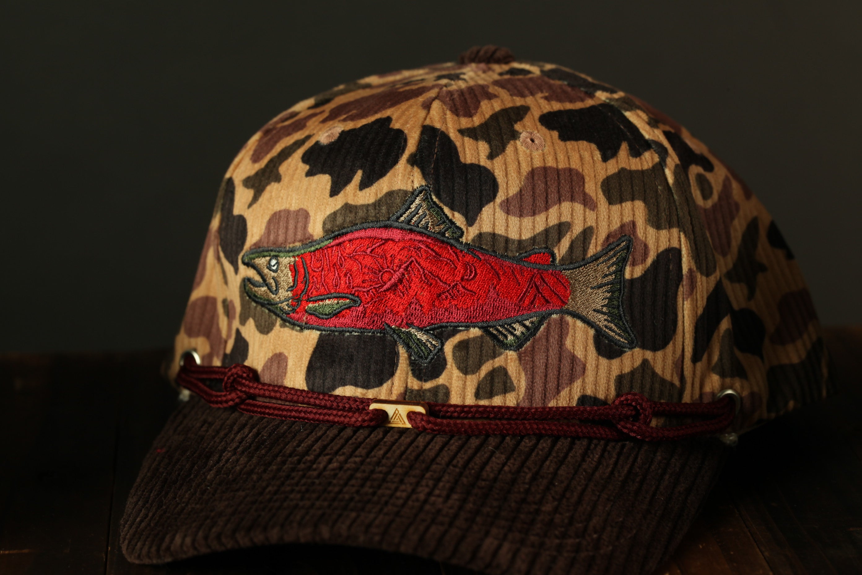 A camouflage baseball cap with a red fish embroidered on it.