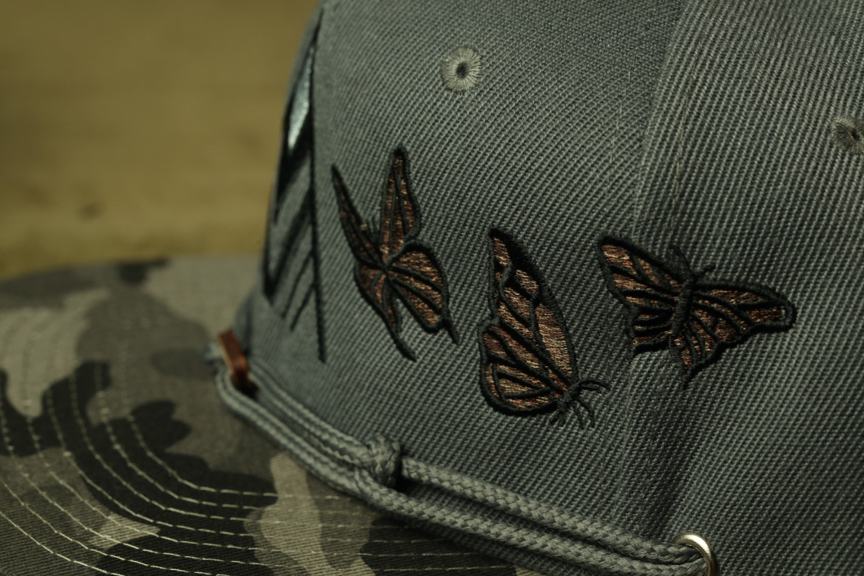 A close-up view of a gray baseball cap with three embroidered butterflies on the front.