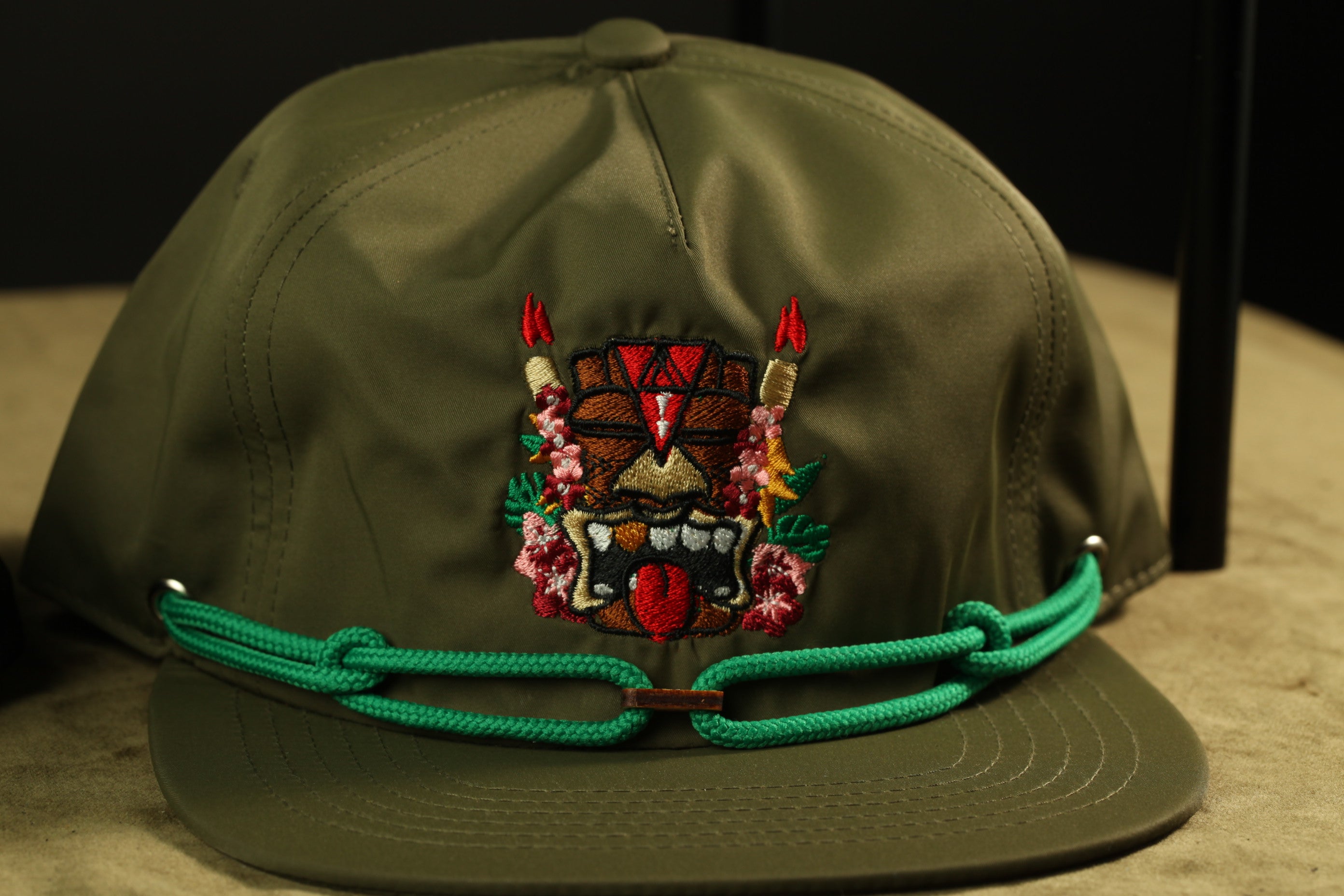 A close-up image of a green baseball cap with a colorful, embroidered design on the front.