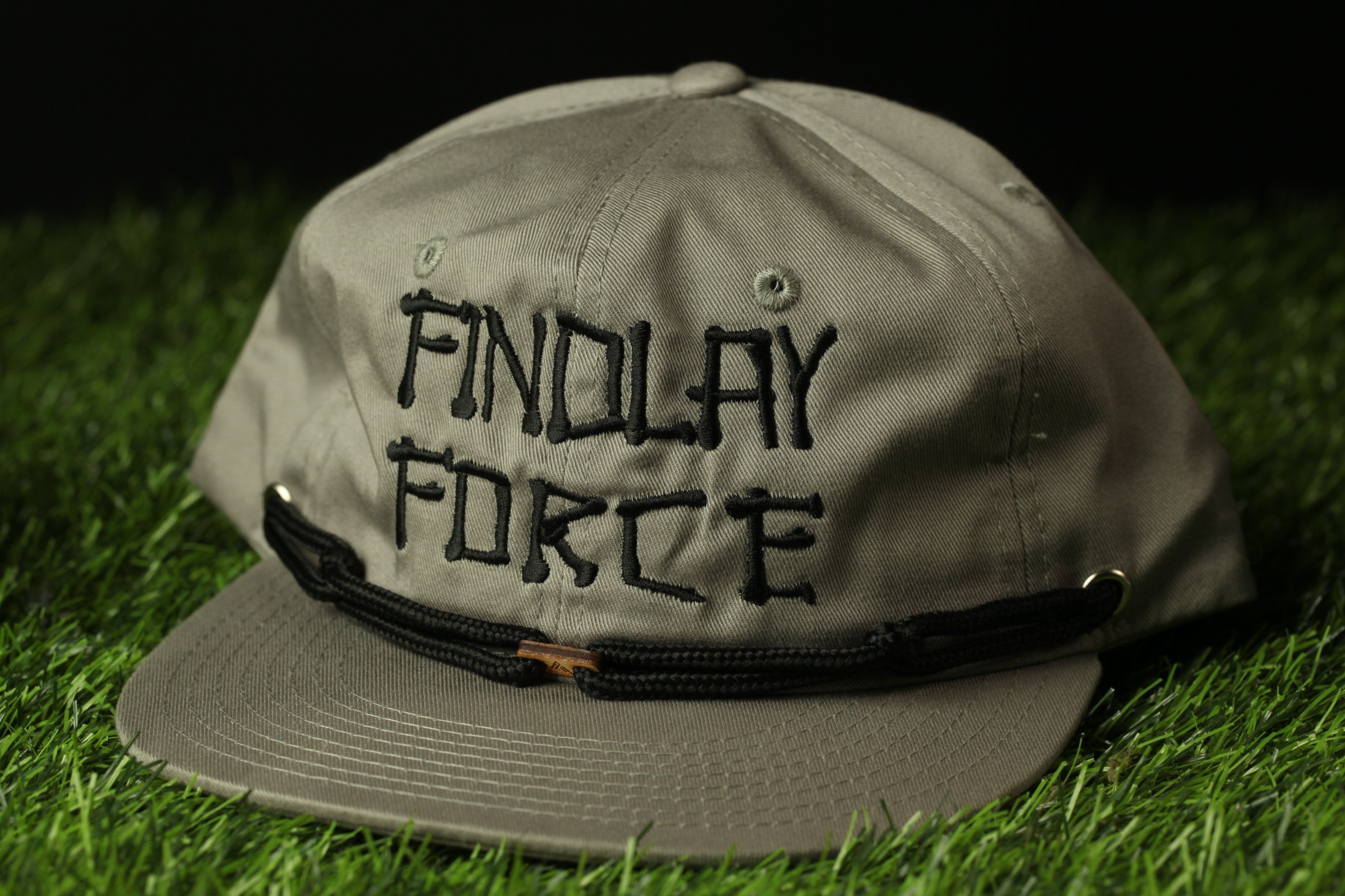 A gray baseball cap with the text "FINDOLAY FORCE" printed on it, sitting on a grassy surface.
