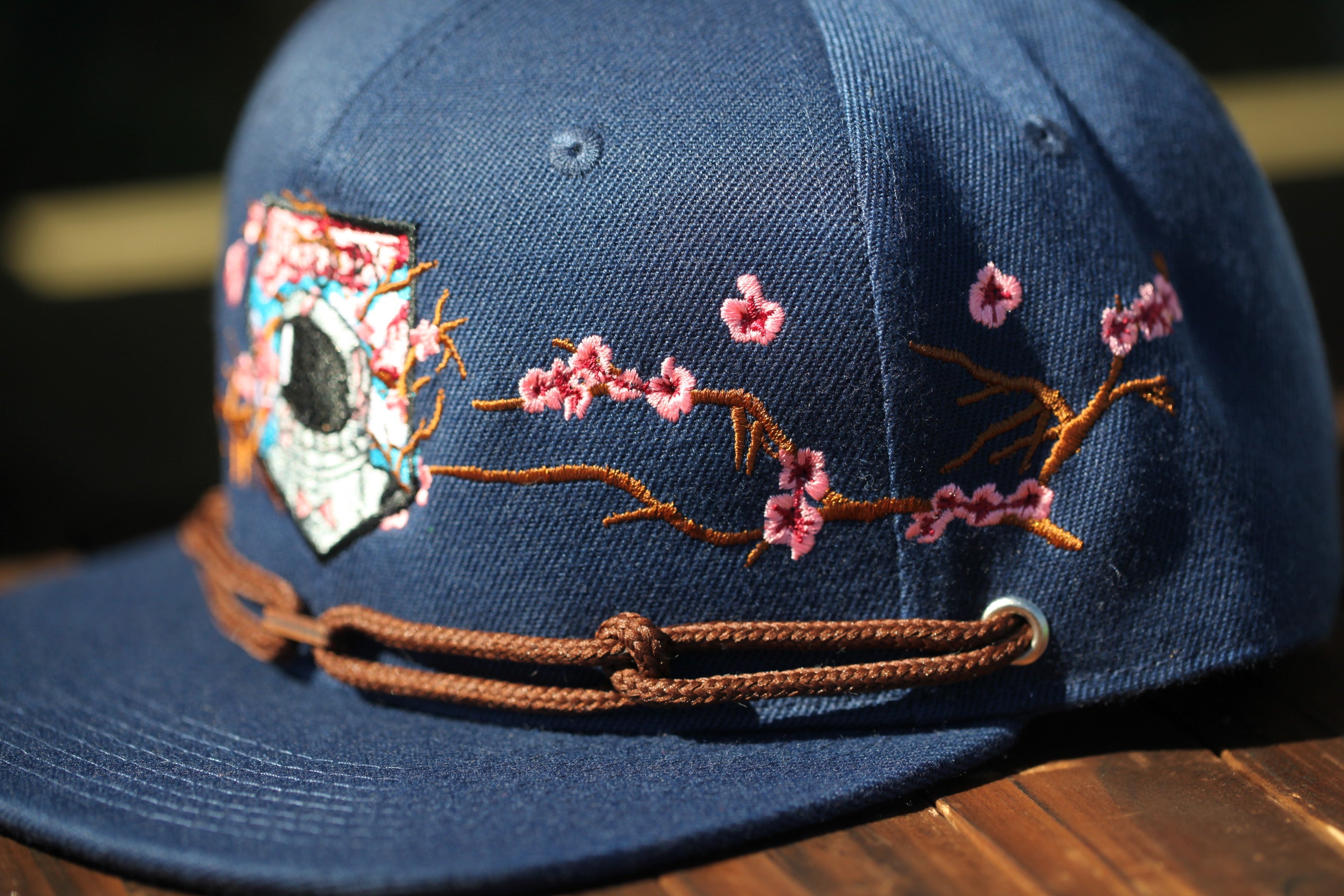 A close-up view of a blue baseball cap with a floral embroidered design on the front.