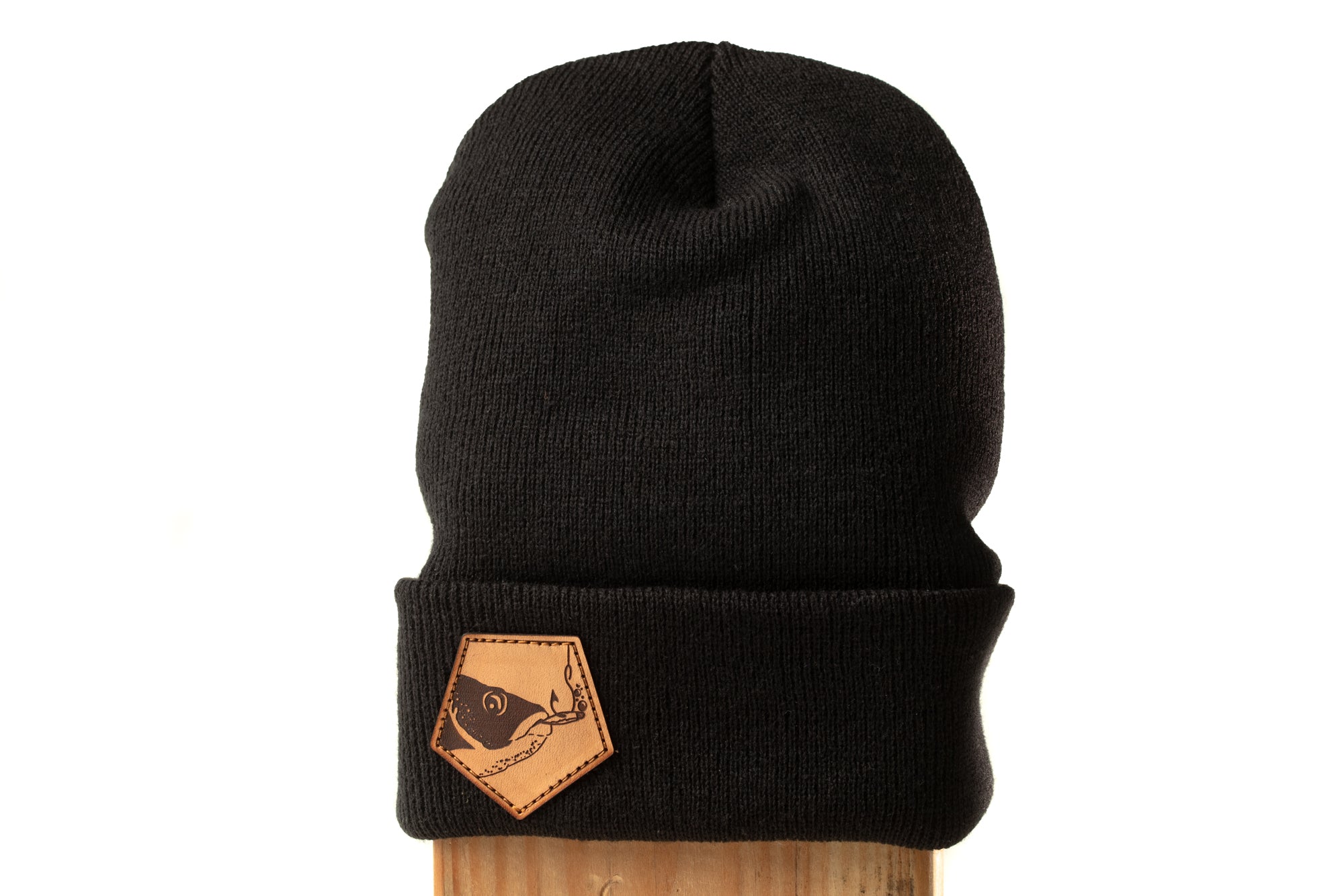 A black knit beanie with a leather patch on the front.