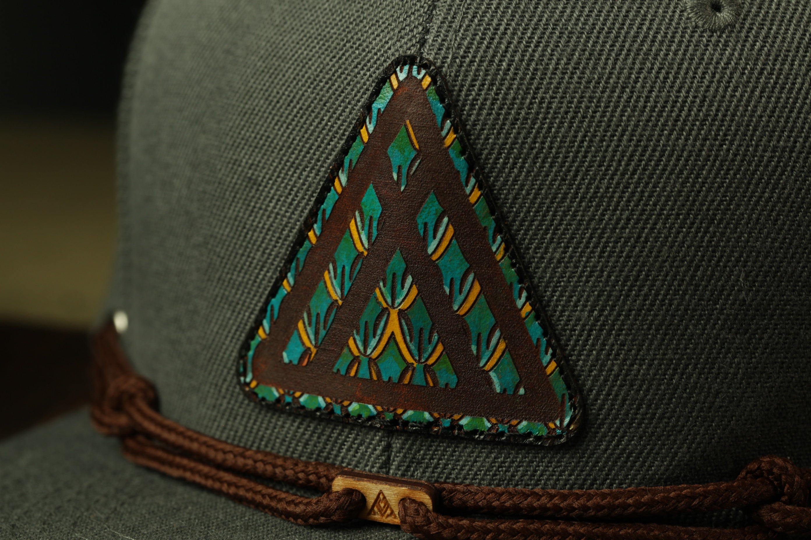 A close-up view of a gray baseball cap with a triangular patch featuring a colorful geometric design.