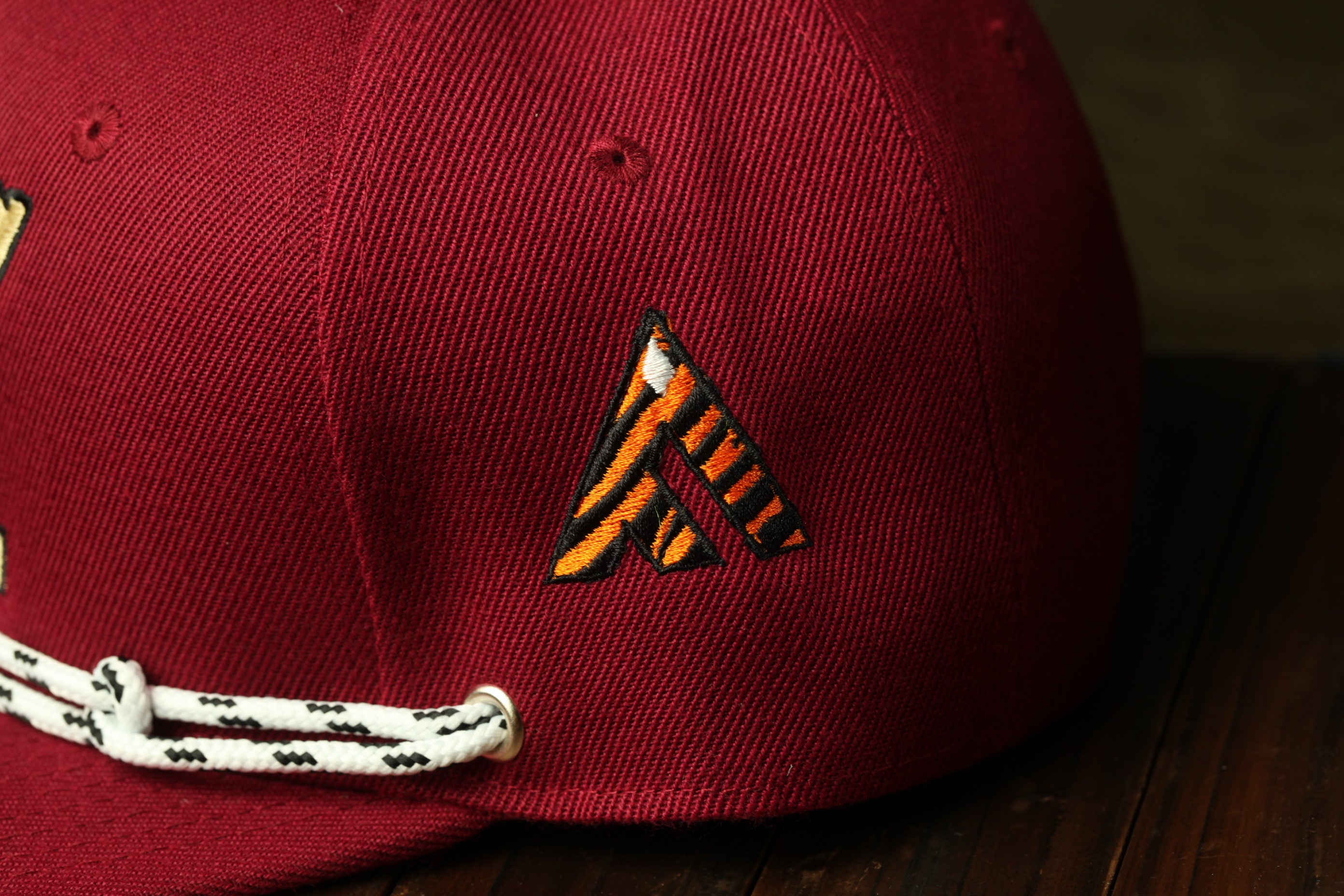 A close-up view of a red baseball cap with a black and orange logo on the front.