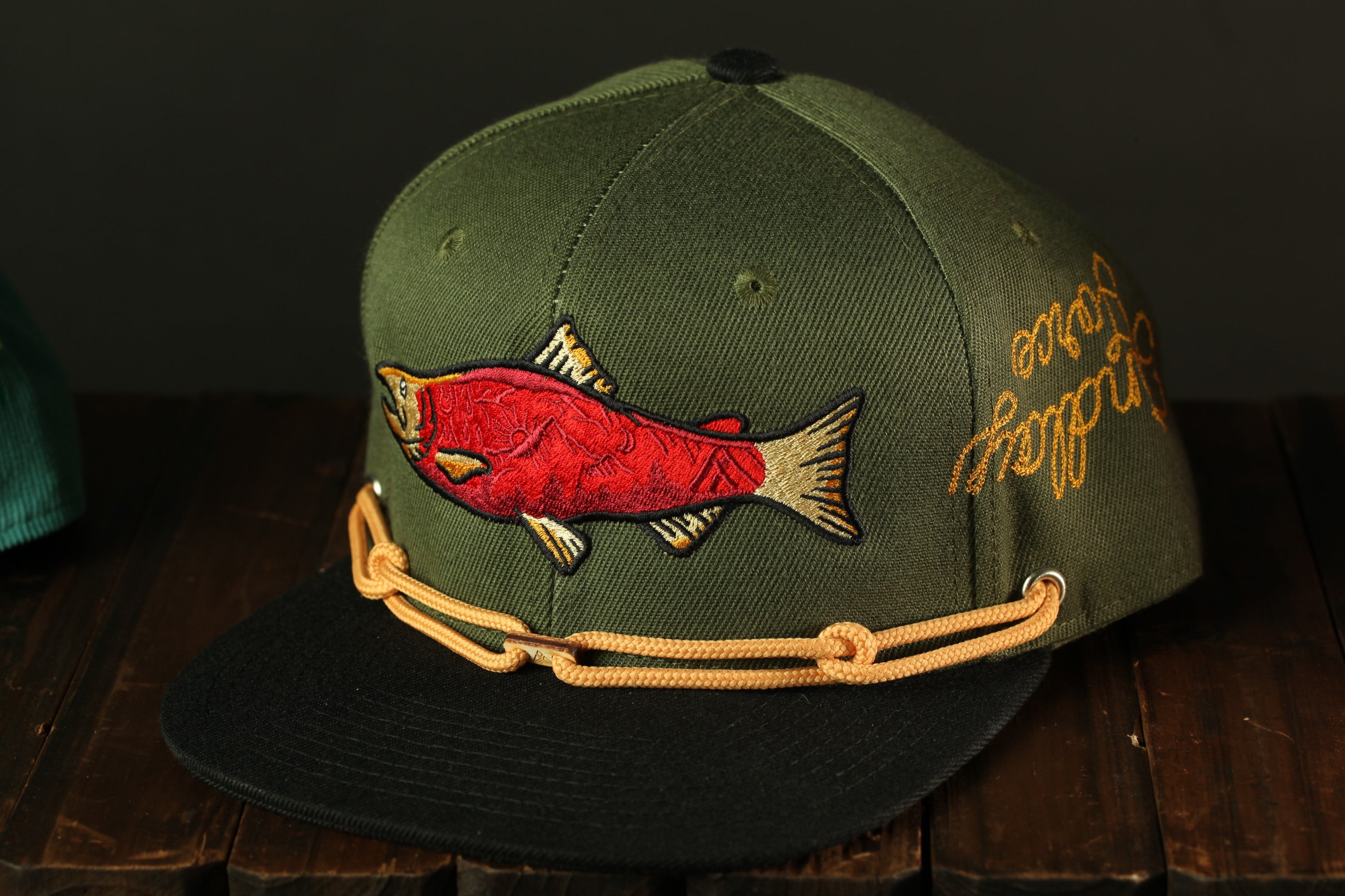 A green baseball cap with a red fish embroidered on it, sitting on a wooden surface.