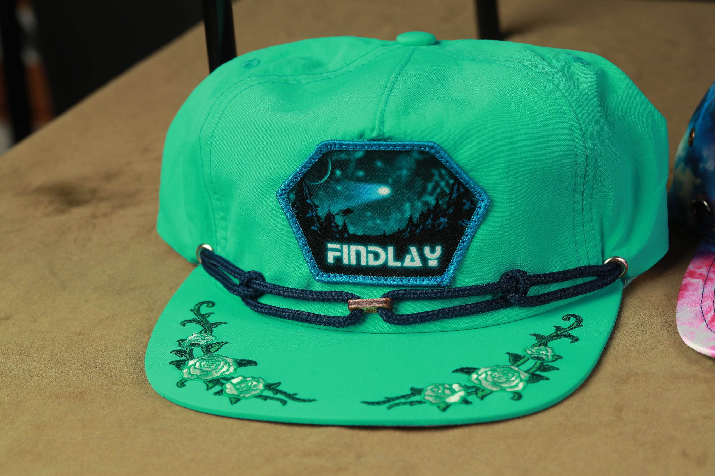 A green baseball cap with a patch on the front and floral designs on the brim.