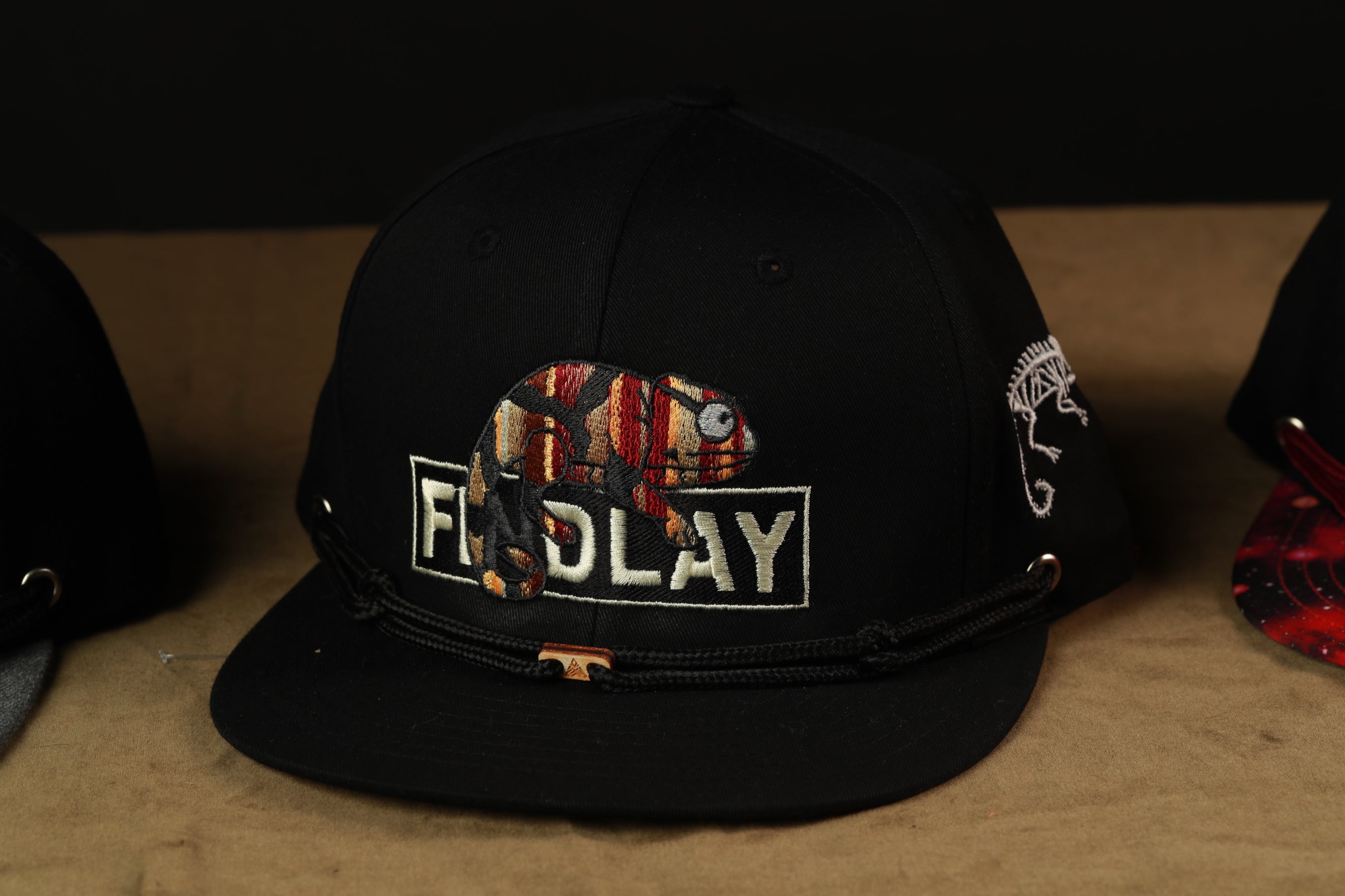 A black baseball cap with a colorful graphic and text on it, sitting on a surface.