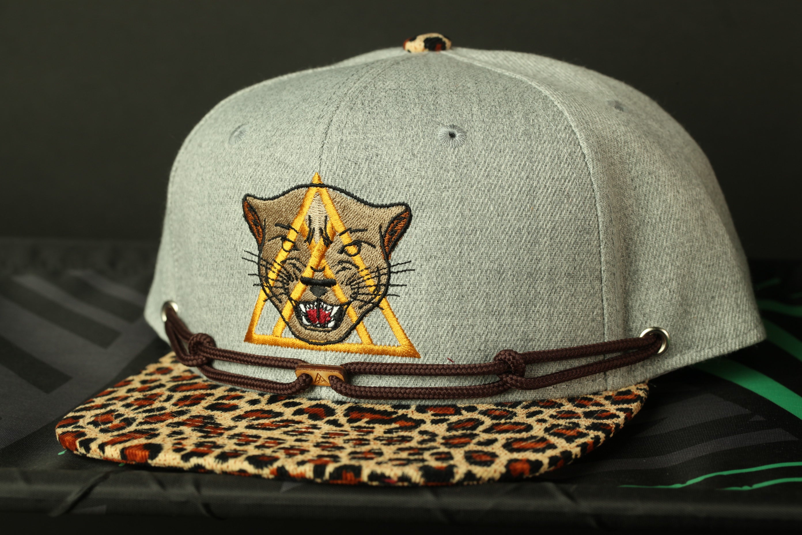 A gray baseball cap with a leopard print pattern and a yellow triangle design on the front.