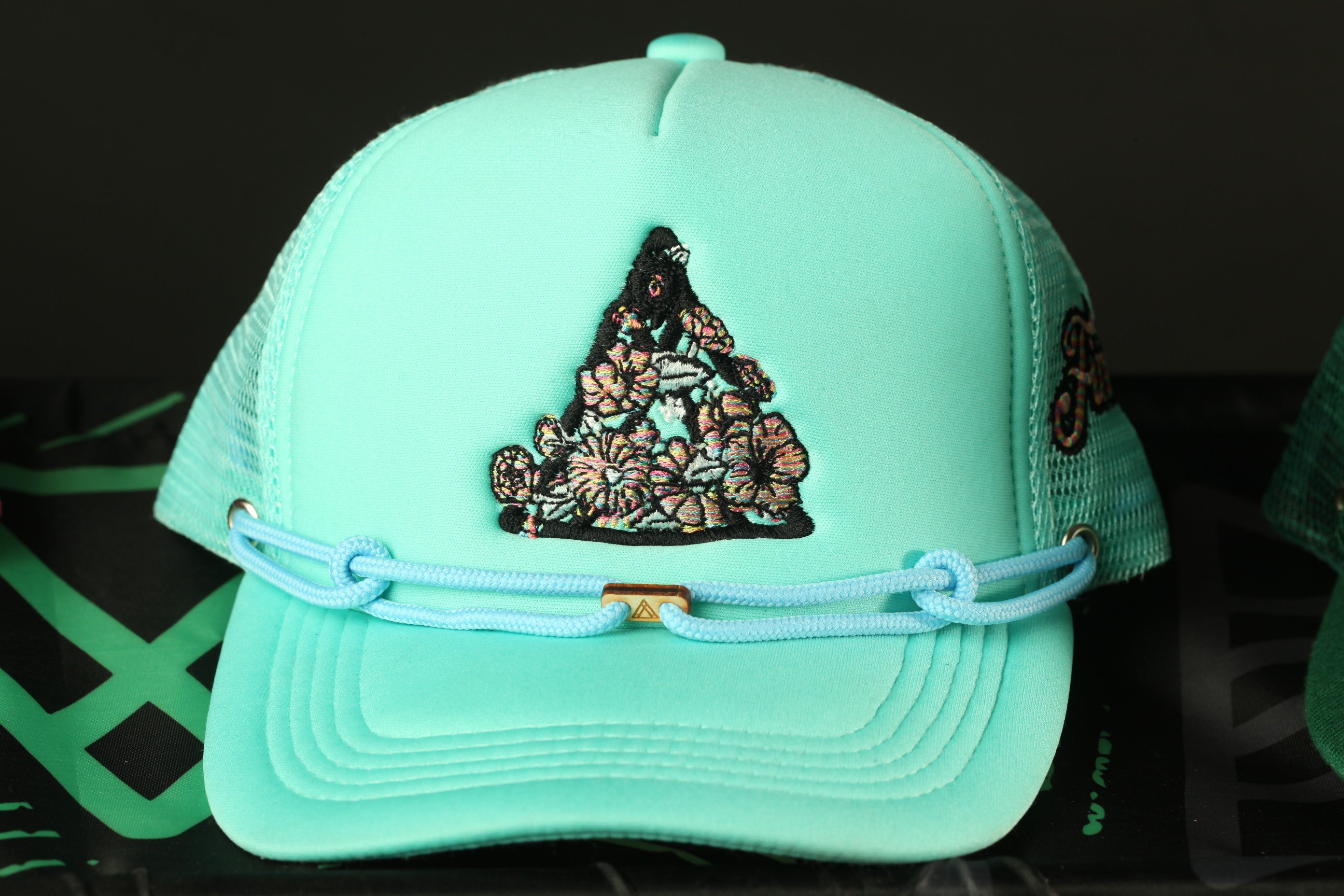 A turquoise baseball cap with a floral embroidered design on the front.