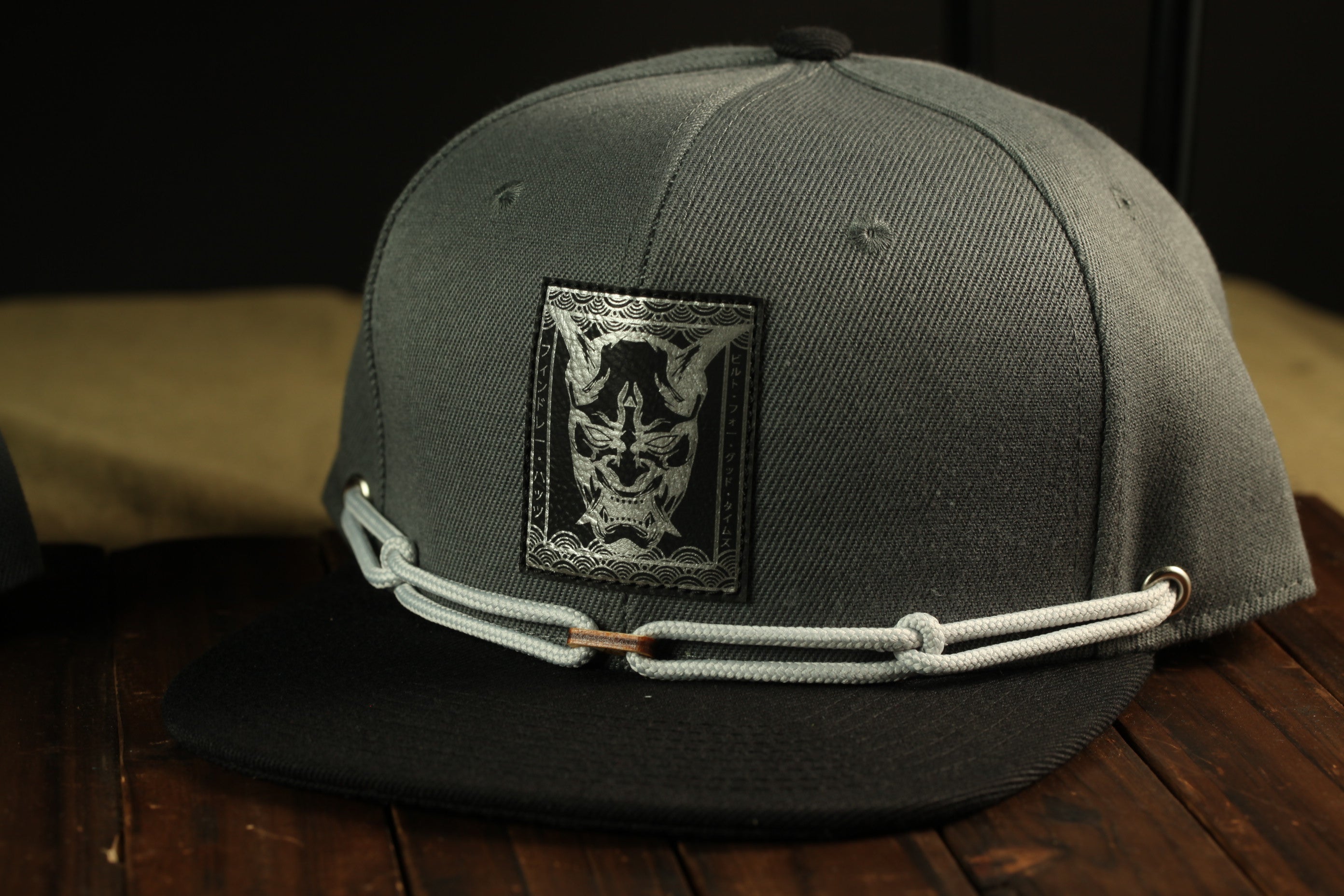 A gray baseball cap with a black and white graphic patch on the front, sitting on a wooden surface.