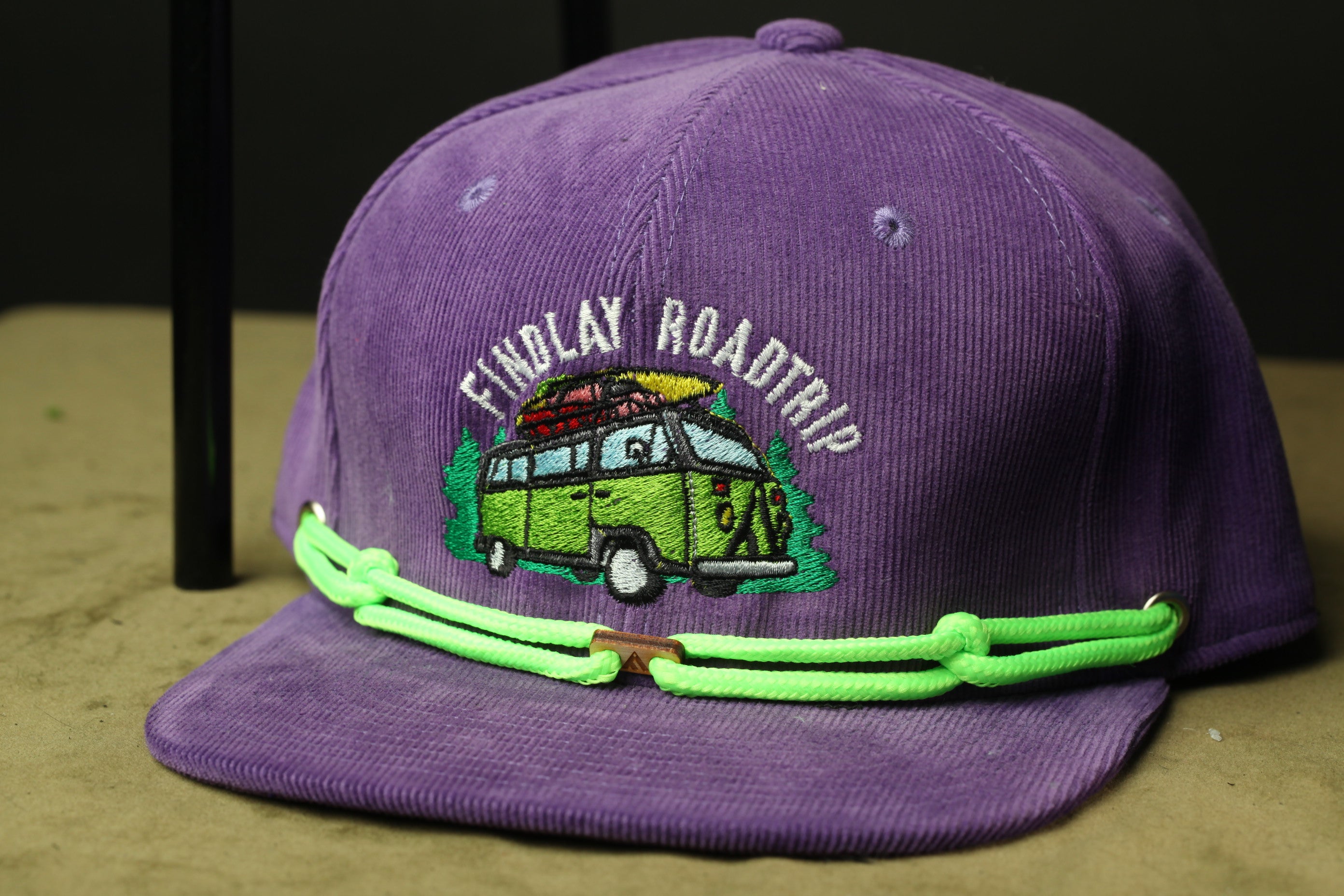 A purple baseball cap with a graphic of a van and the text "Findlay Road Trip" printed on it.