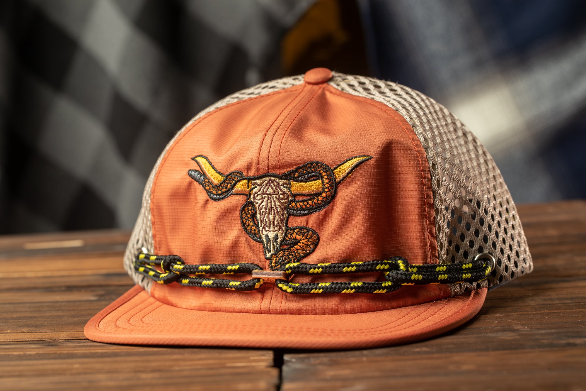 An orange baseball cap with a mesh back and a black and yellow chain strap, placed on a wooden surface.