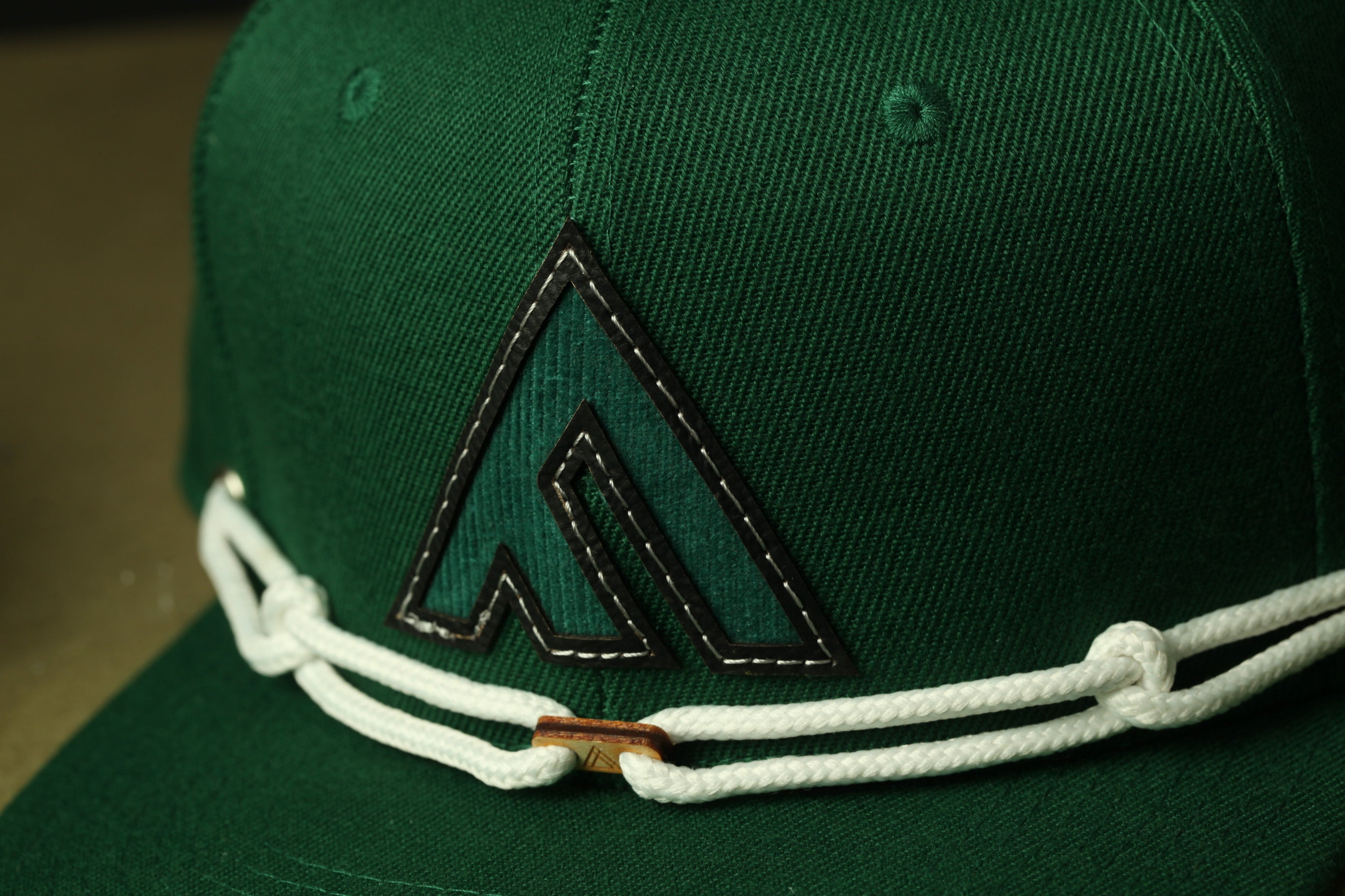 A close-up view of a green baseball cap with a black and white logo on the front.