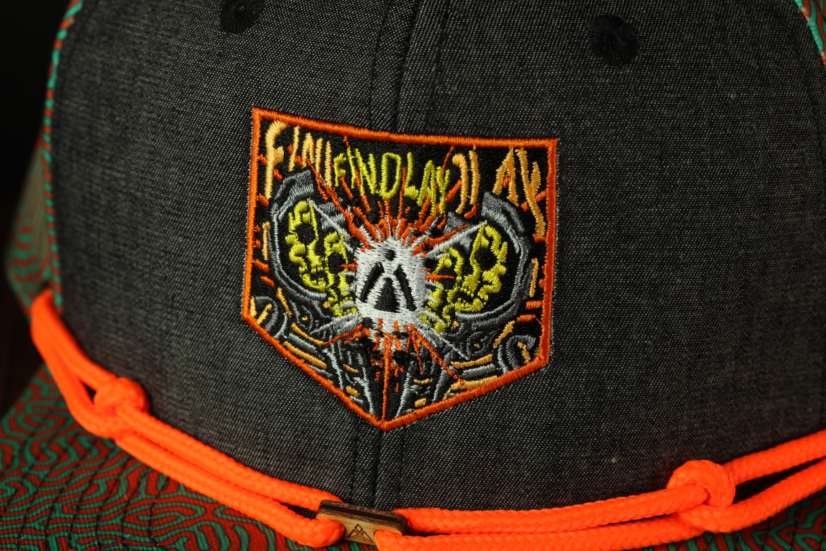 a close-up view of a black baseball cap with an orange and yellow embroidered patch on the front.