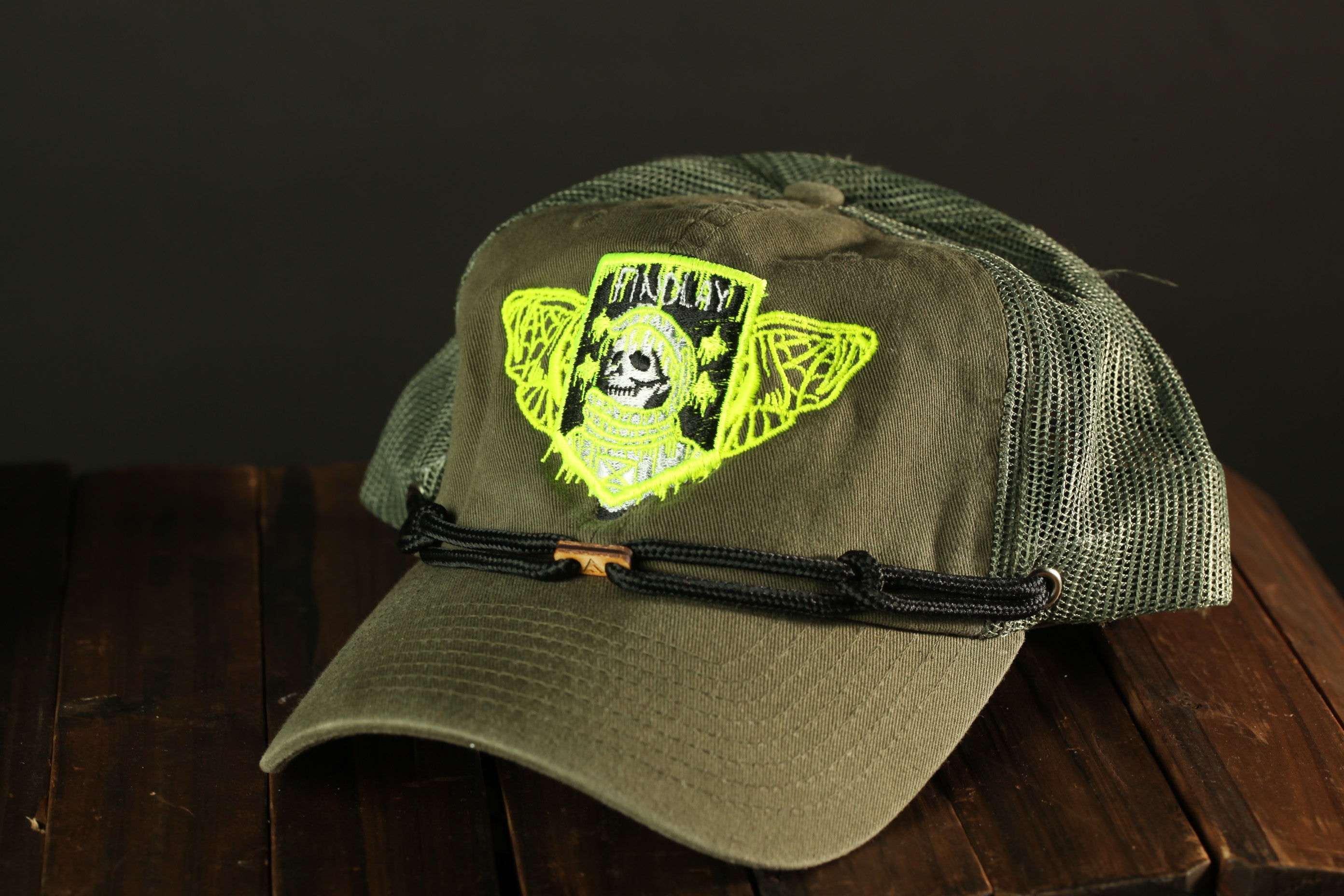 A green baseball cap with a skull and crossbones design on the front, sitting on a wooden surface.