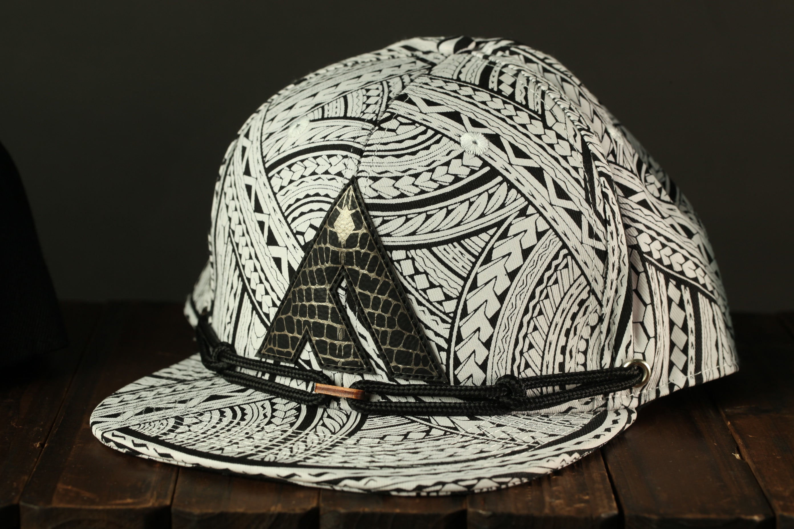 A black and white patterned baseball cap with a distinctive triangular logo on the front, resting on a wooden surface.