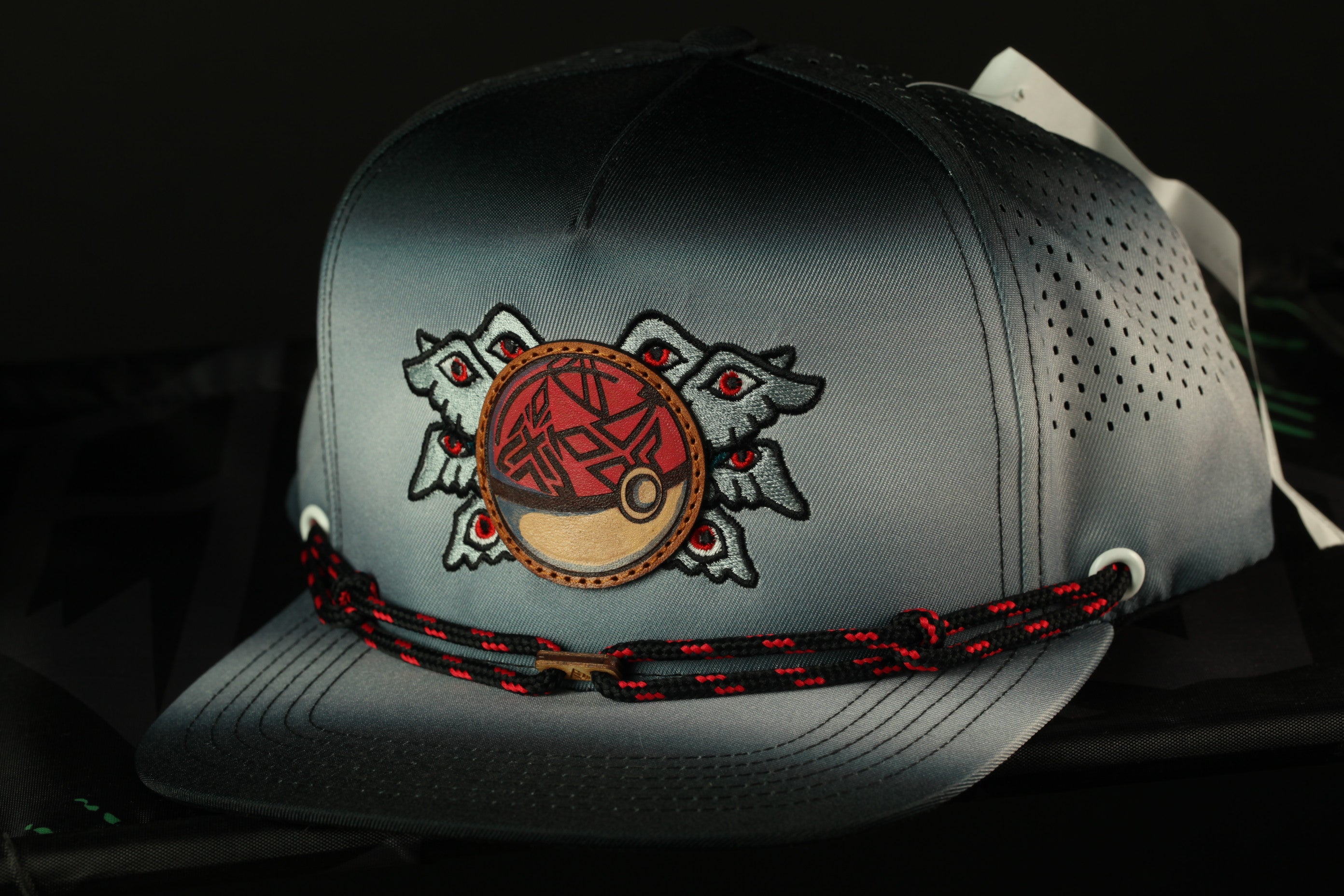 A gray baseball cap with a red and black design on the front, featuring a circular emblem with a stylized face and a fish-like motif.
