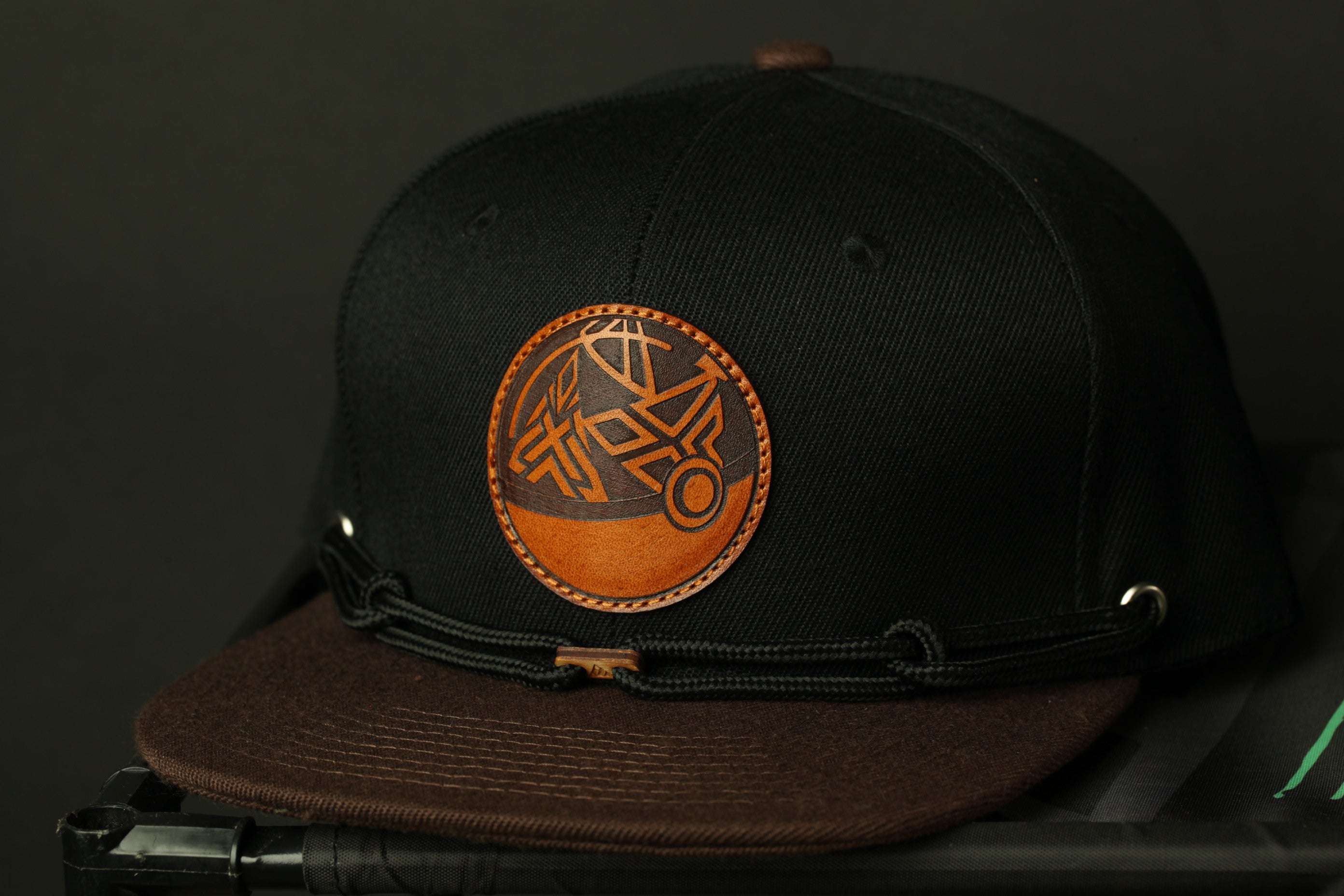 A black baseball cap with a brown leather logo on the front.