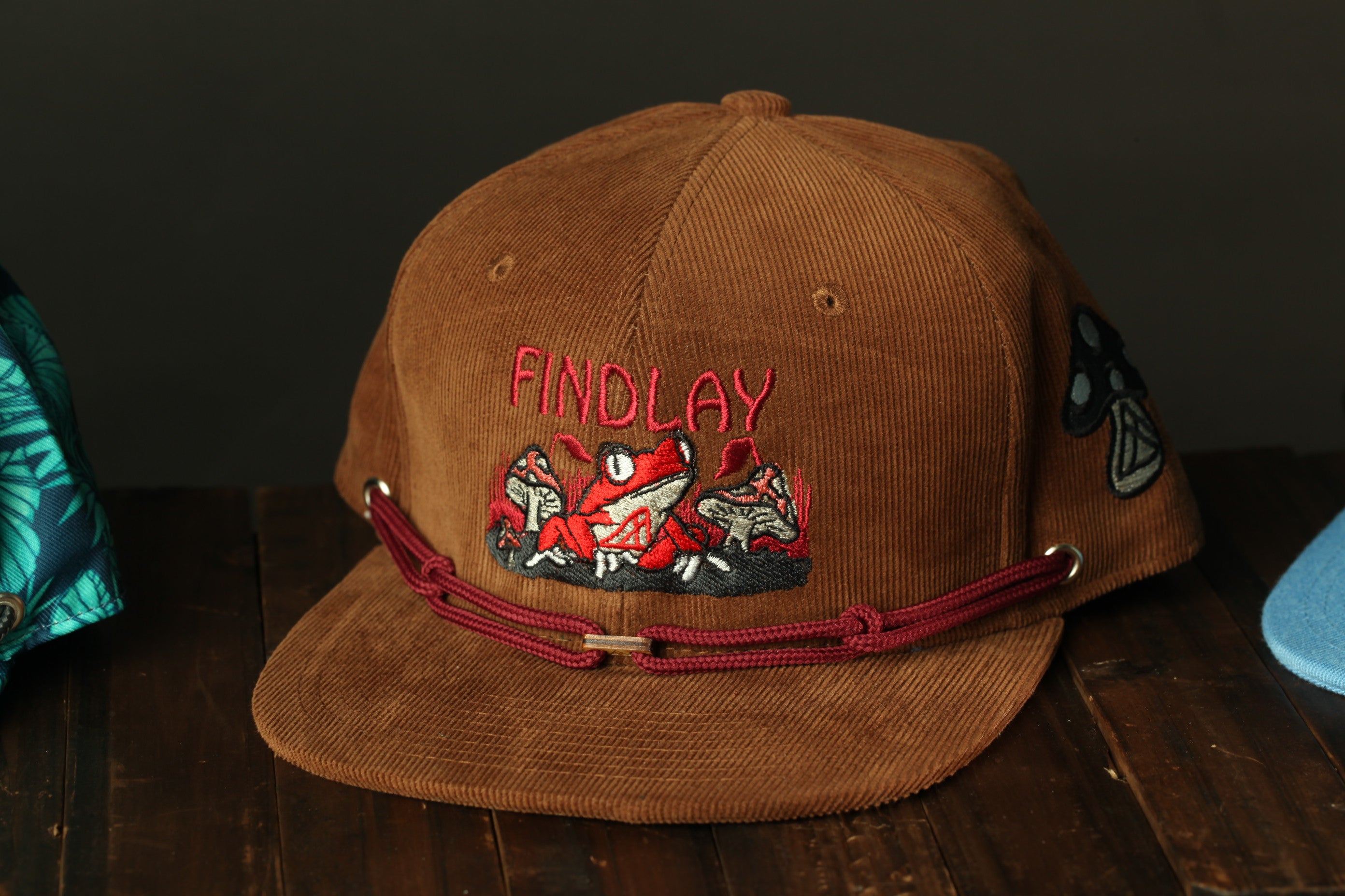 A brown baseball cap with a red and black embroidered design, featuring the word "FINDlay" on the front.