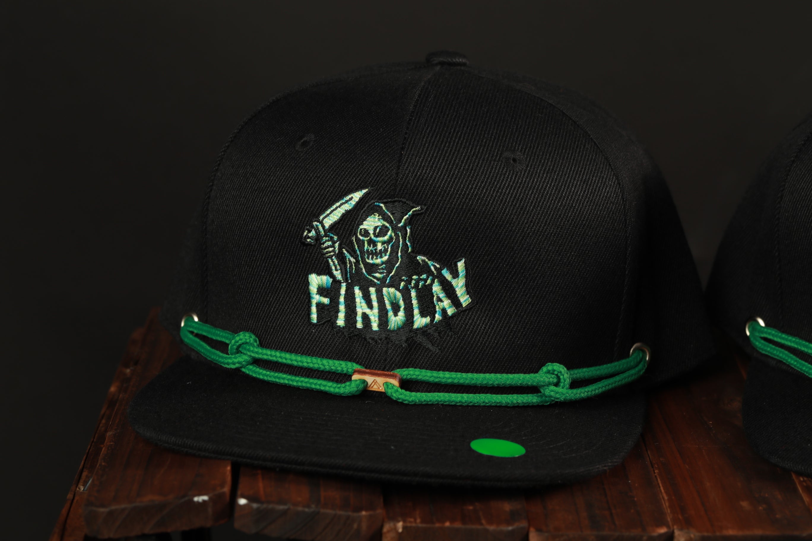 A black baseball cap with a green string and a skull and crossbones design on the front.