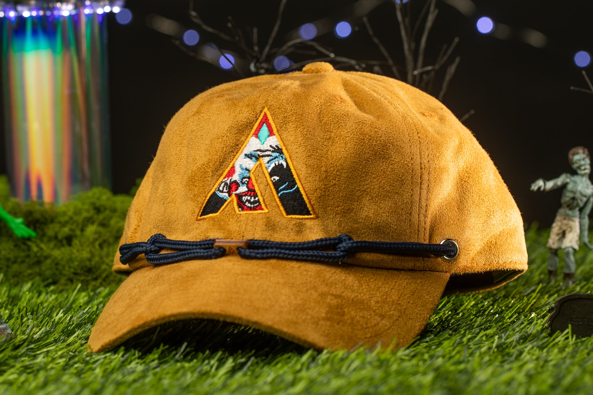 A brown baseball cap with a unique logo is placed on a grassy surface, with a blurred background featuring a figure and some colorful objects.