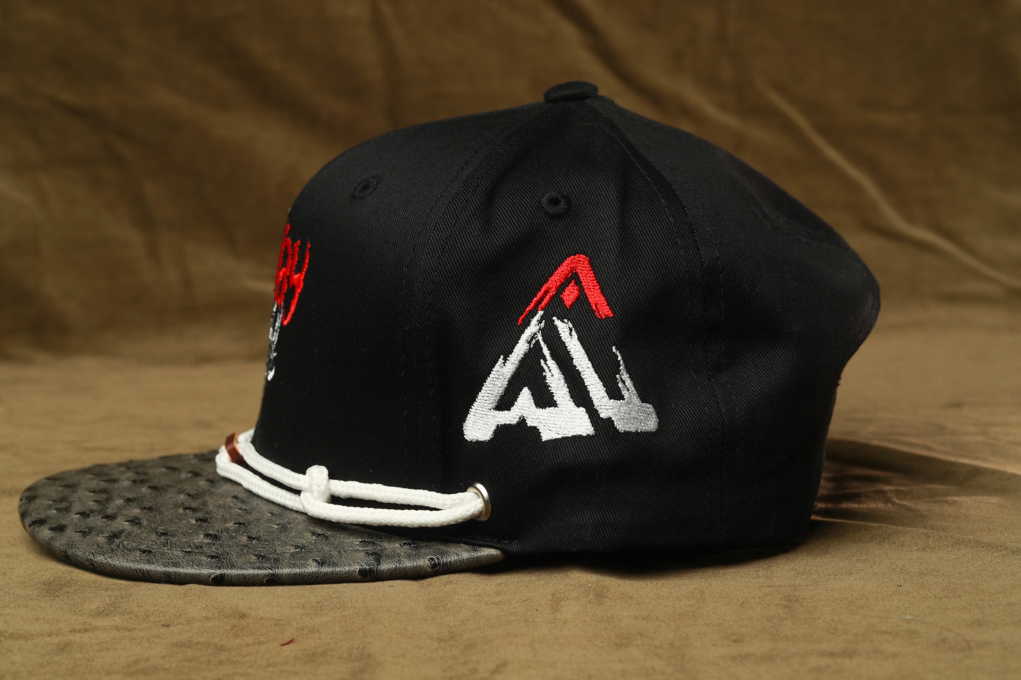 A black baseball cap with a white and red logo on the side, sitting on a brown surface.