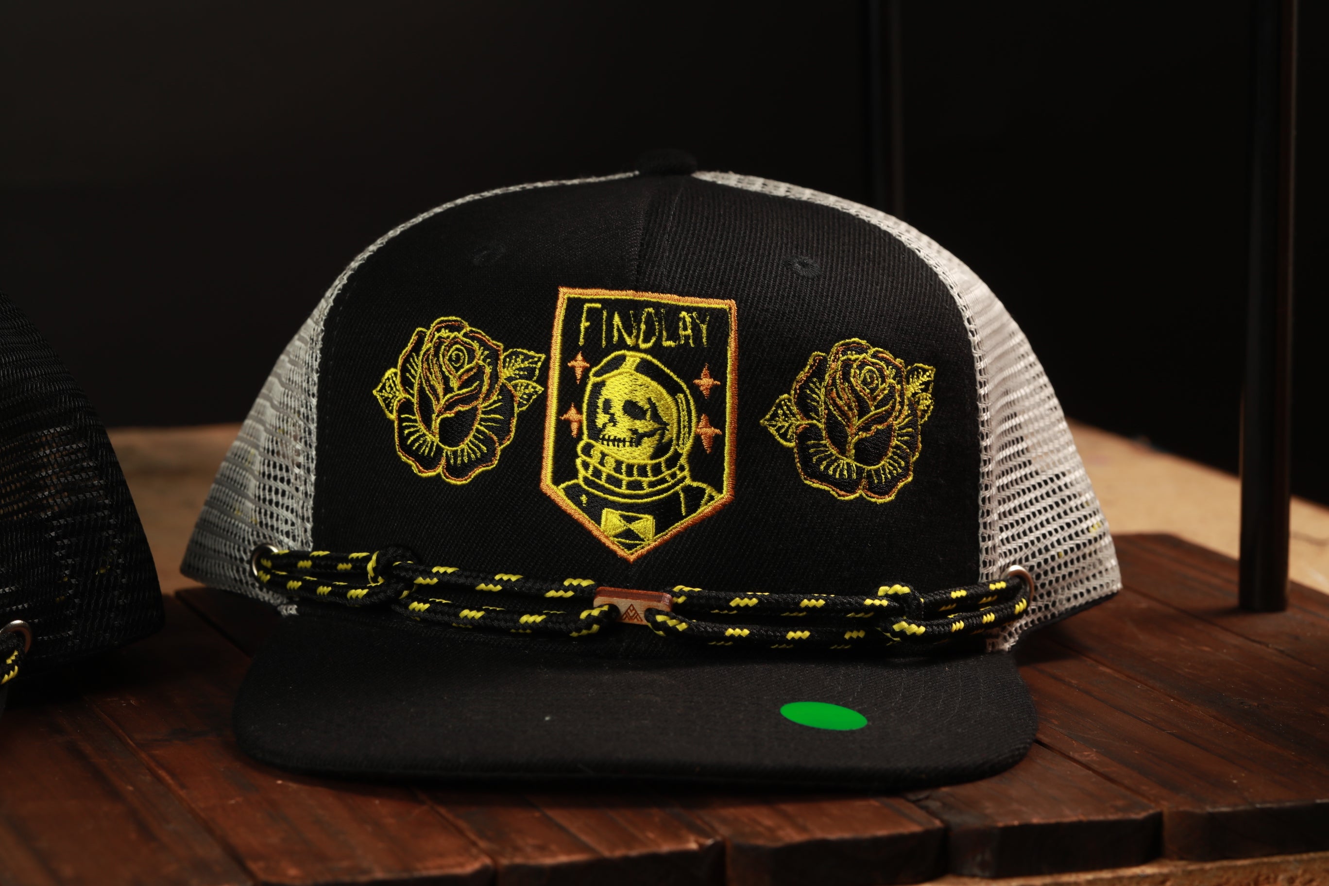 A black baseball cap with a skull and rose embroidered on it, sitting on a wooden surface.