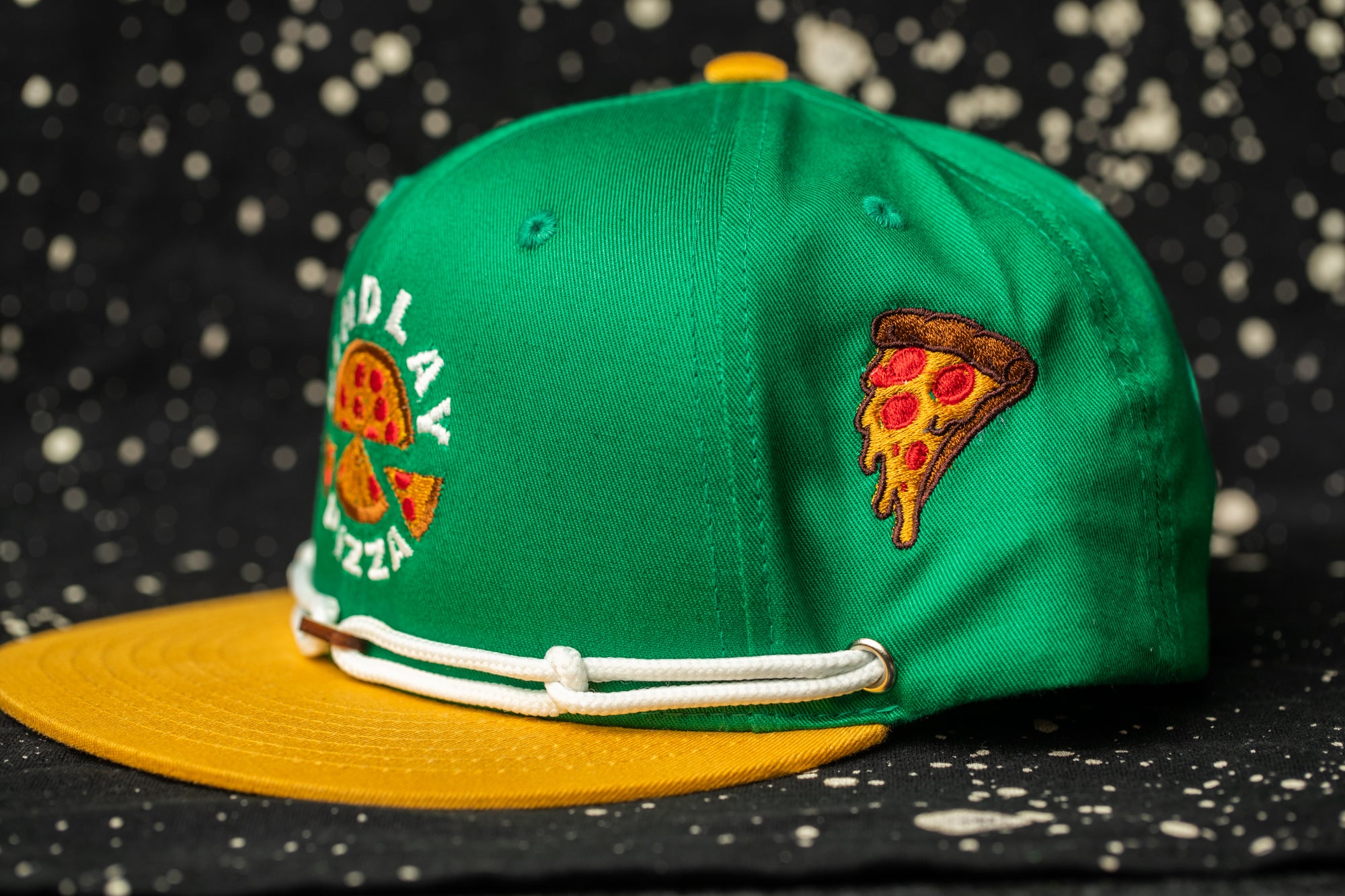 A green baseball cap with a yellow brim, featuring a pizza slice embroidered on the side.