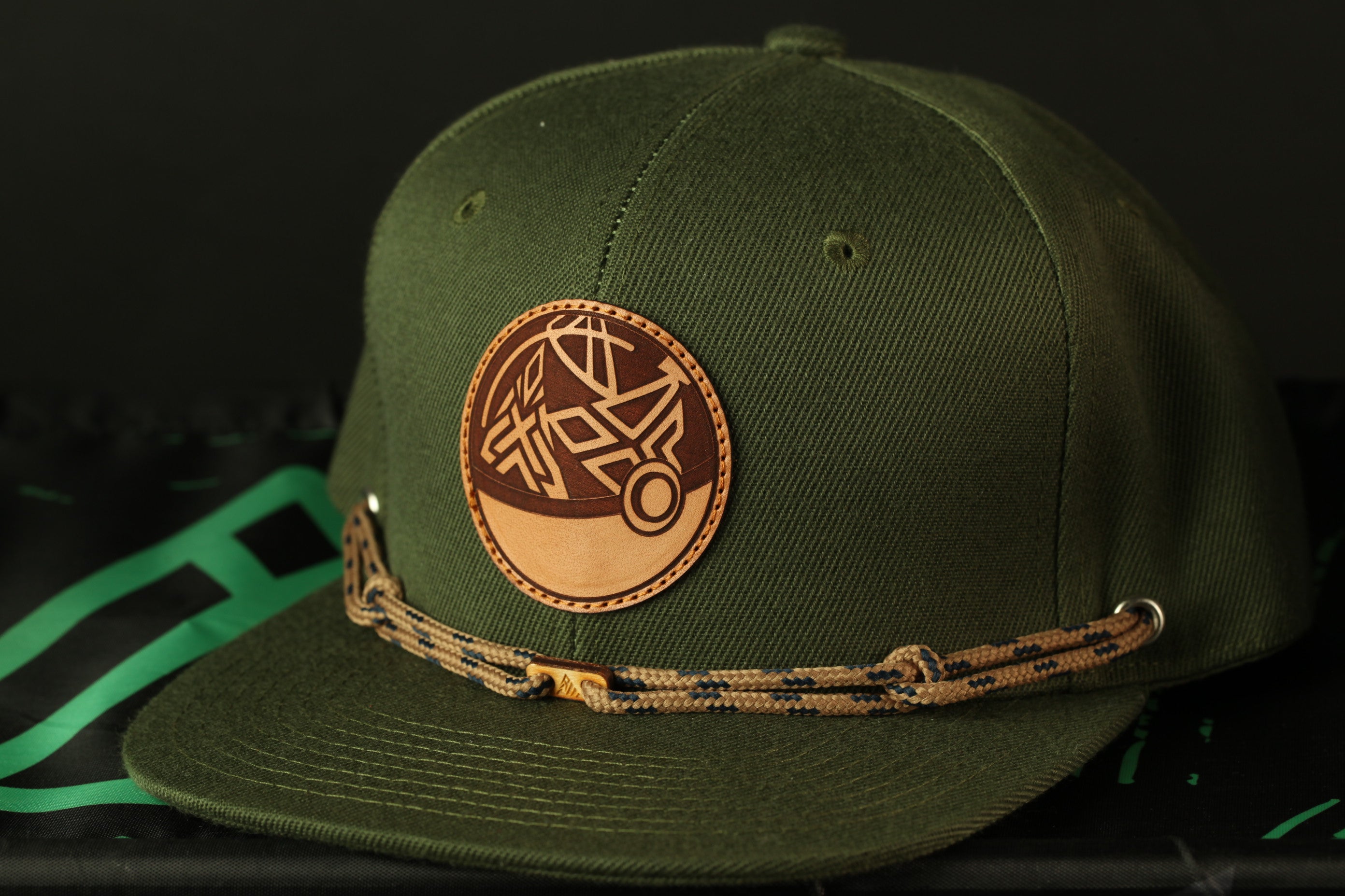 A green baseball cap with a leather patch and a braided strap.