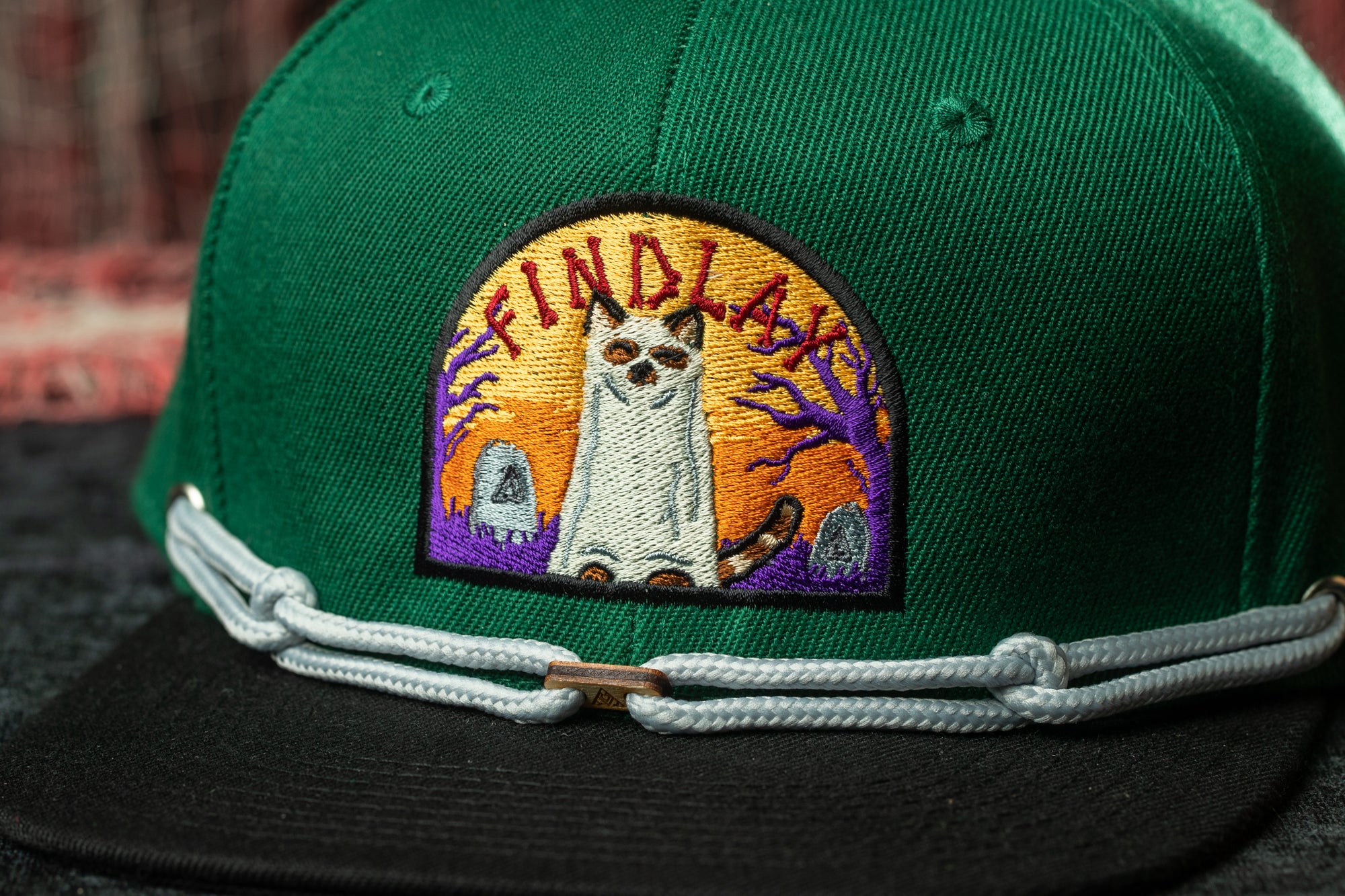A close-up of a green baseball cap with a patch featuring a cat and the text "FIND A" on it.