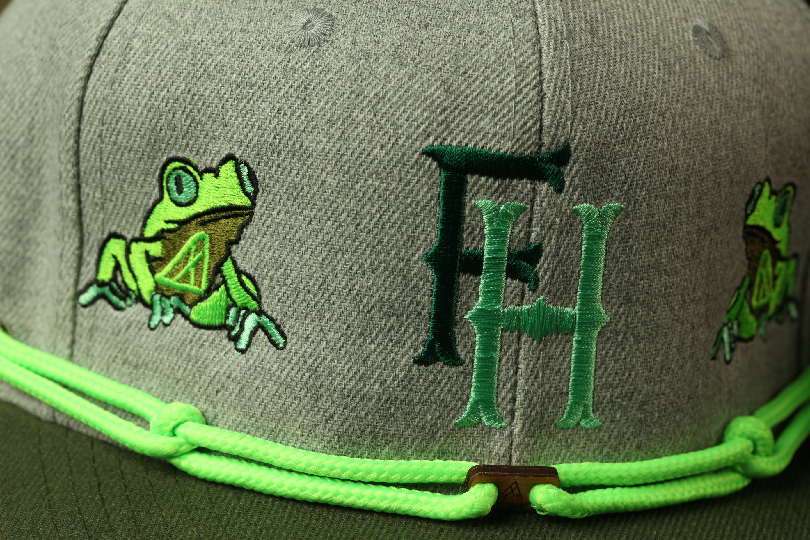 A gray baseball cap with green frog embroidery and the letters "FH" on the front.