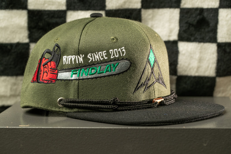 A green baseball cap with a black brim and a black strap, featuring embroidered text and graphics on the front.